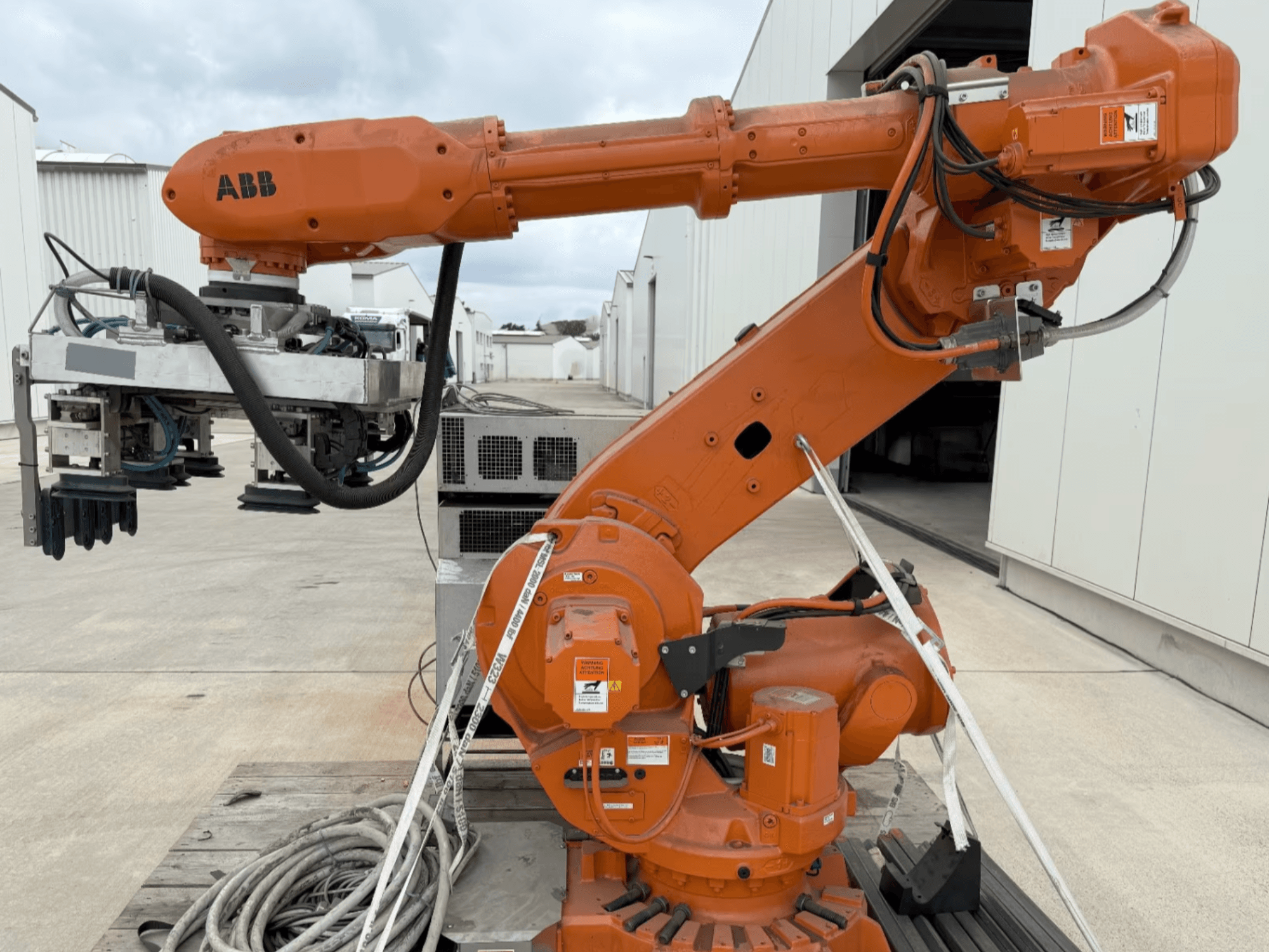 ABB RB 6600-130/3.2 robota roka sānu skatā, ar oranžu robota roku ar satvērēja stiprinājumu un redzamiem vadiem.