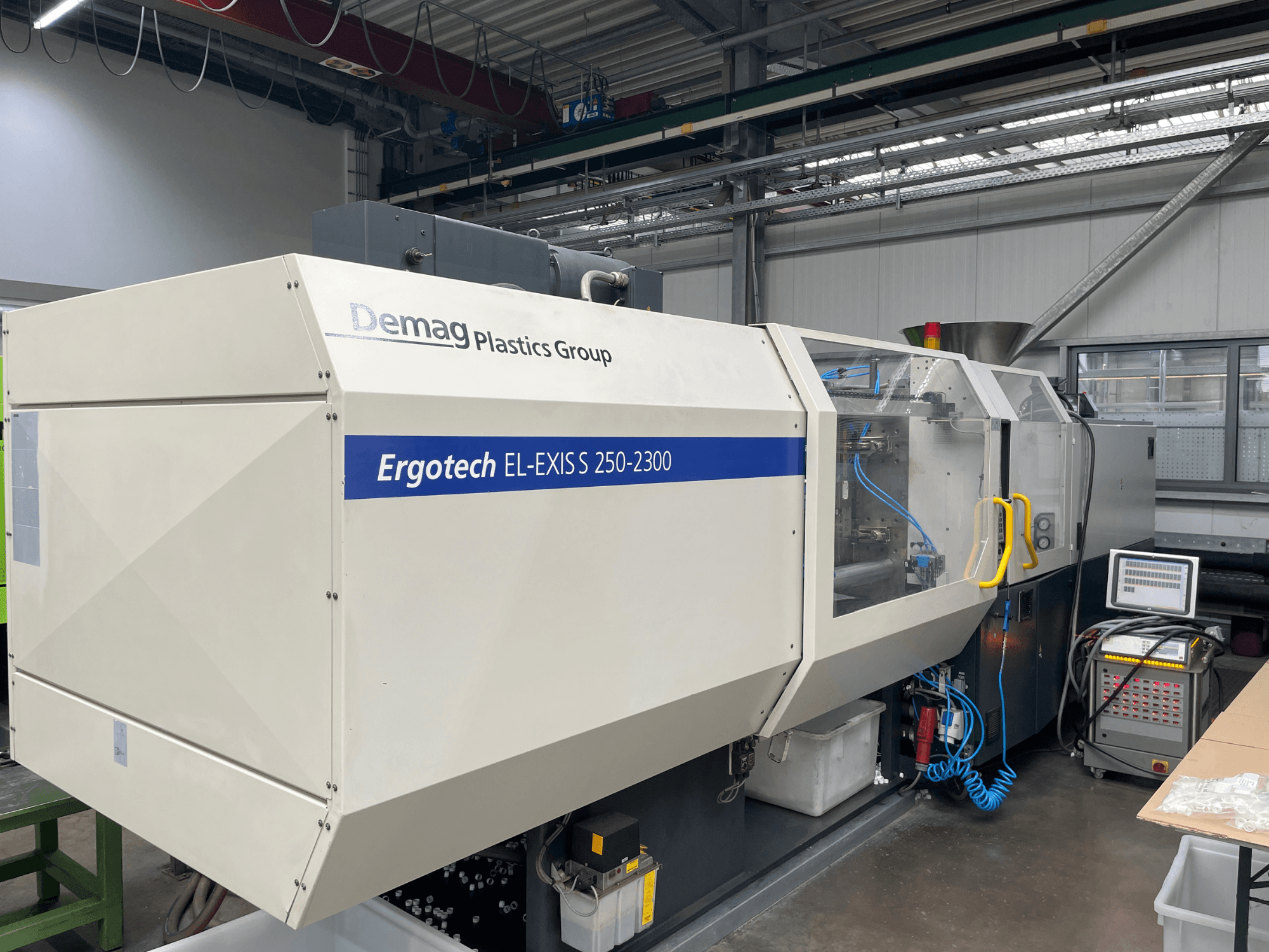 Demag Ergotech EL-EXIS S 250-2300 injekcijas formēšanas iekārta, skats no sāniem, redzams vadības panelis un padeves sistēma.