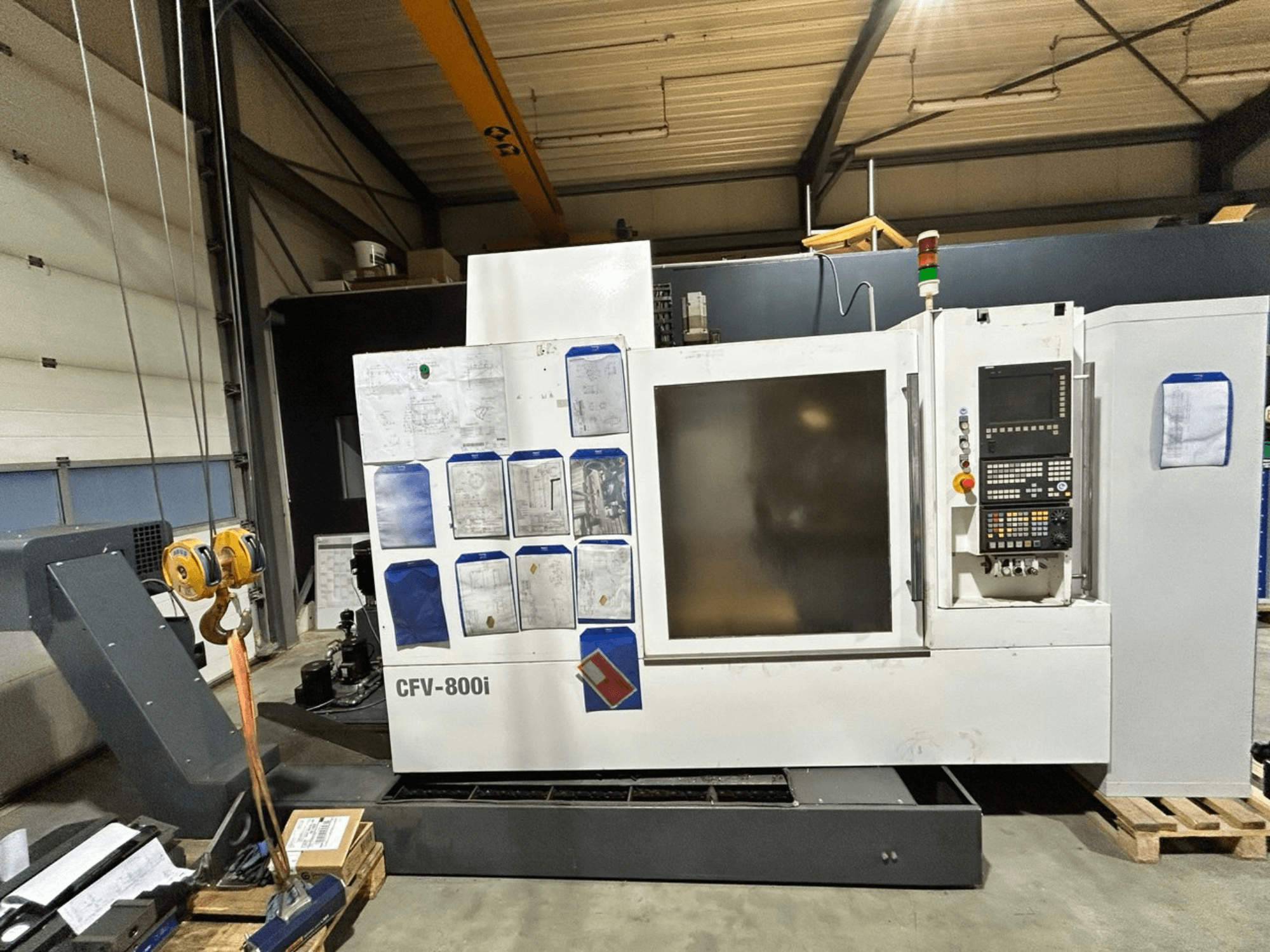 CFV-800i CNC mašīna priekšpusē, ar vadības paneli, dokumentiem sānos un tilta celtni rūpnīcā.