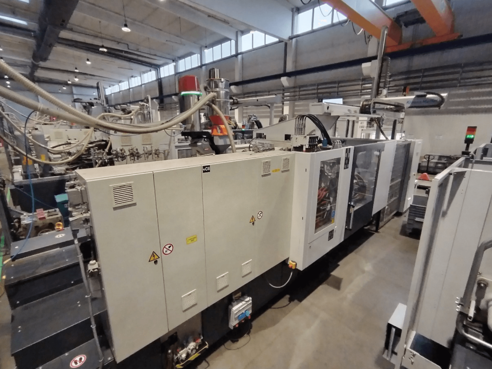 Rūpnieciskā iesmidzināšanas liešanas mašīna, kas parādīta no sānu skata, ar vadības paneli un drošības brīdinājumiem. Zīmols: Nav zināms.