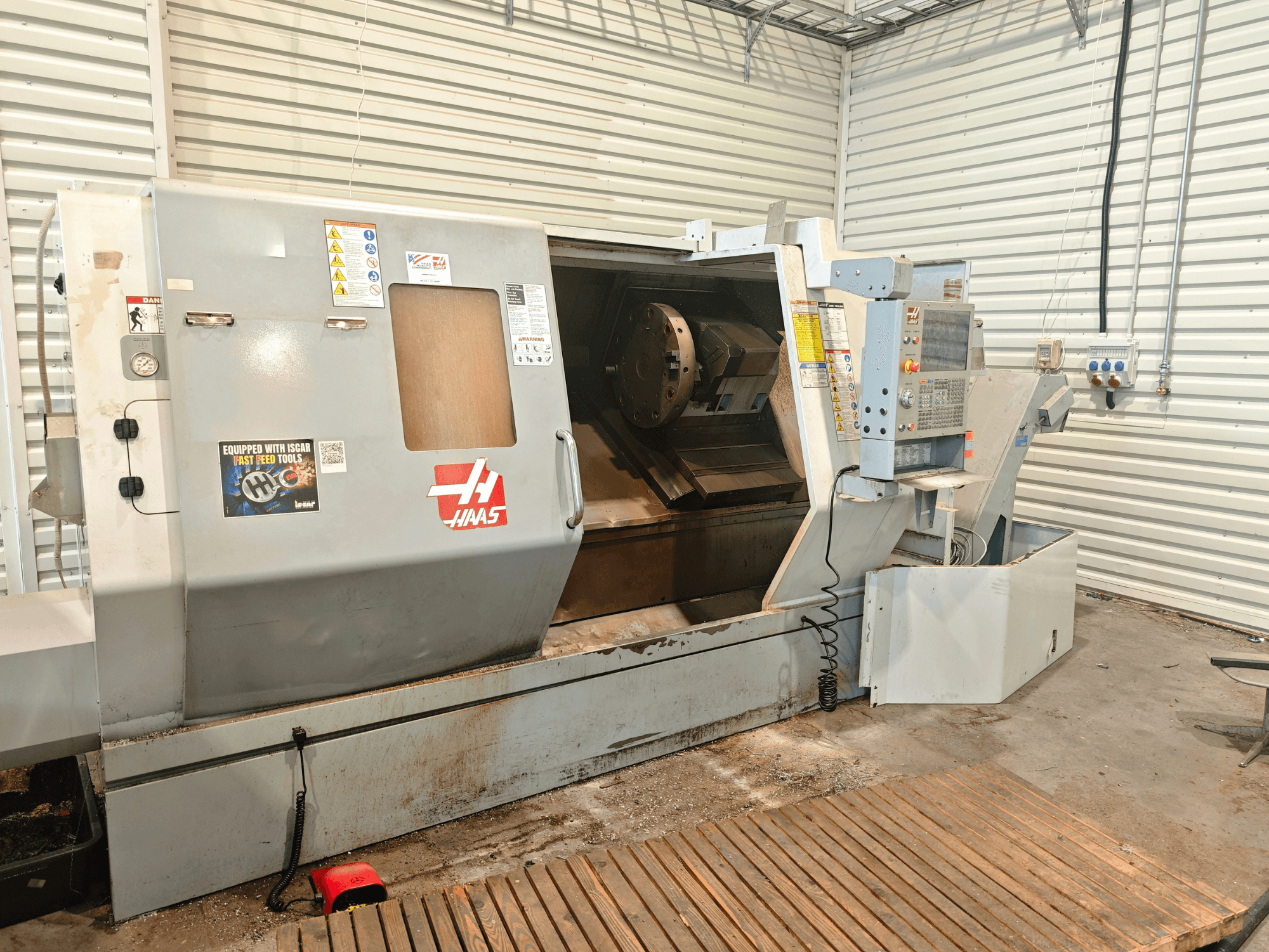 Haas SL-40HE horizontālā virpošanas mašīna, skats no priekšpuses, kurā redzams vadības panelis, darba zona un drošības uzlīmes.