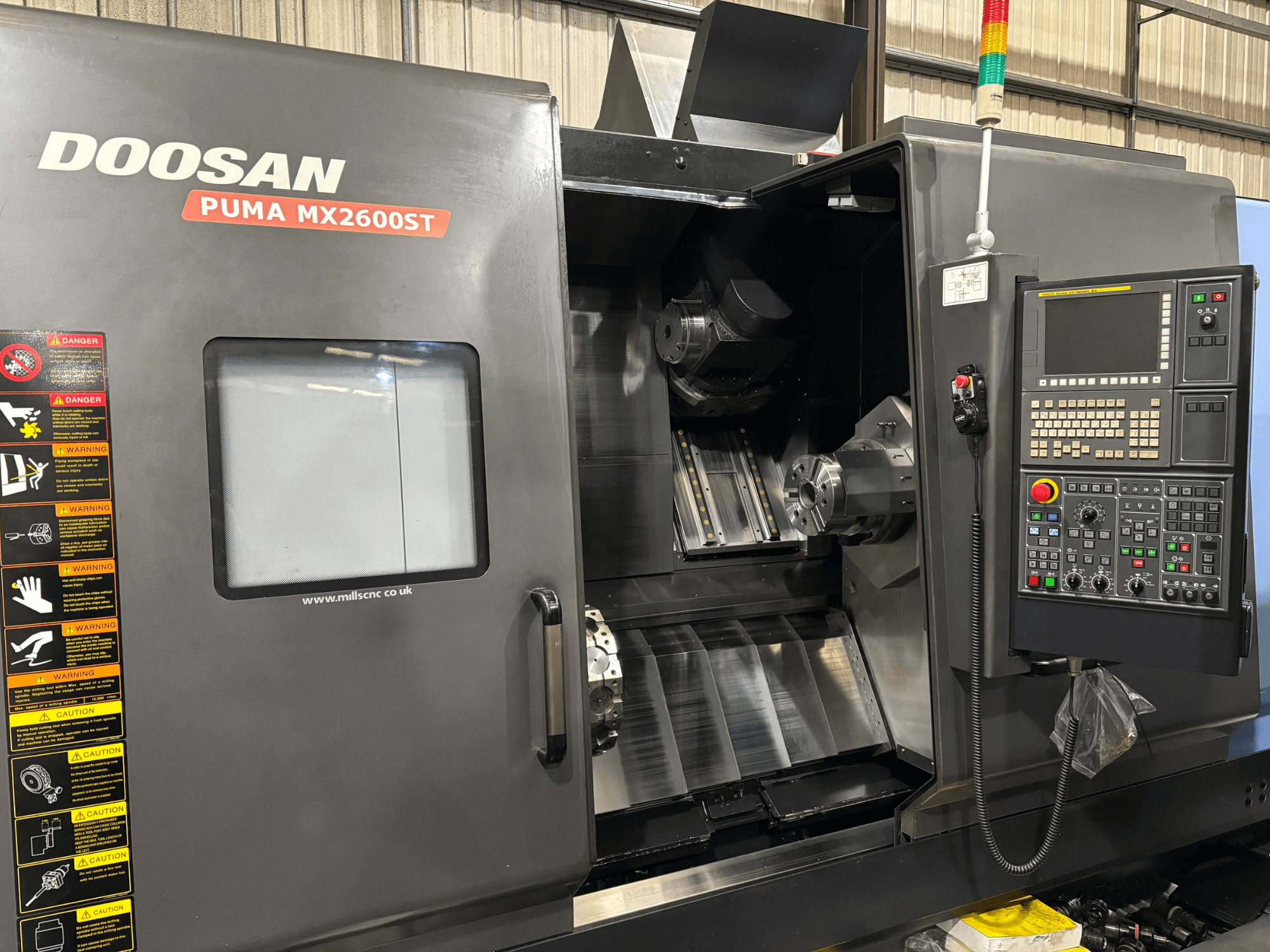 Doosan PUMA MX2600ST CNC virpa, priekšējais skats, kurā redzams vadības panelis, vārpsta un apstrādes zona ar redzamiem drošības brīdinājumiem.