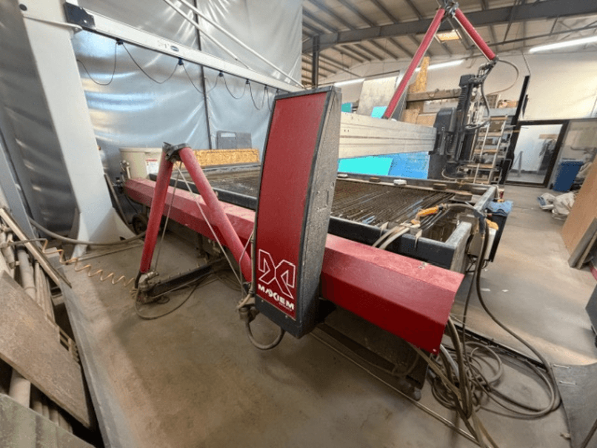 Sarkanā X zīmola ūdensstrūklas griešanas iekārta, skatoties no sāniem, kurā redzamas mehāniskās detaļas un cauruļvadu detaļas.