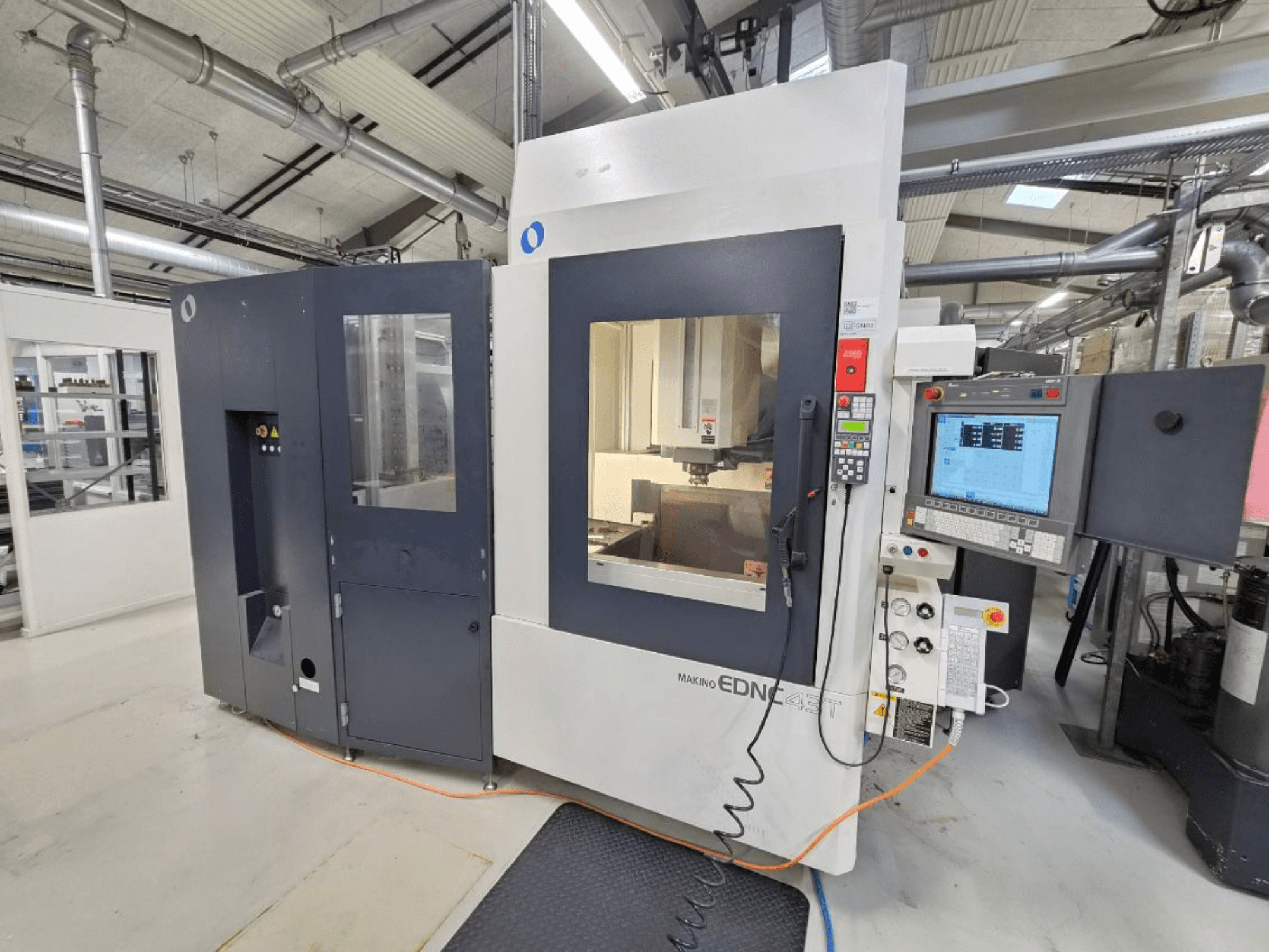 Makino EDNC 43T iegremdēšanas elektroerozijas (EDM) mašīnas skats no priekšpuses, kurā redzams Erowa robots, vadības pultis un darba zona.