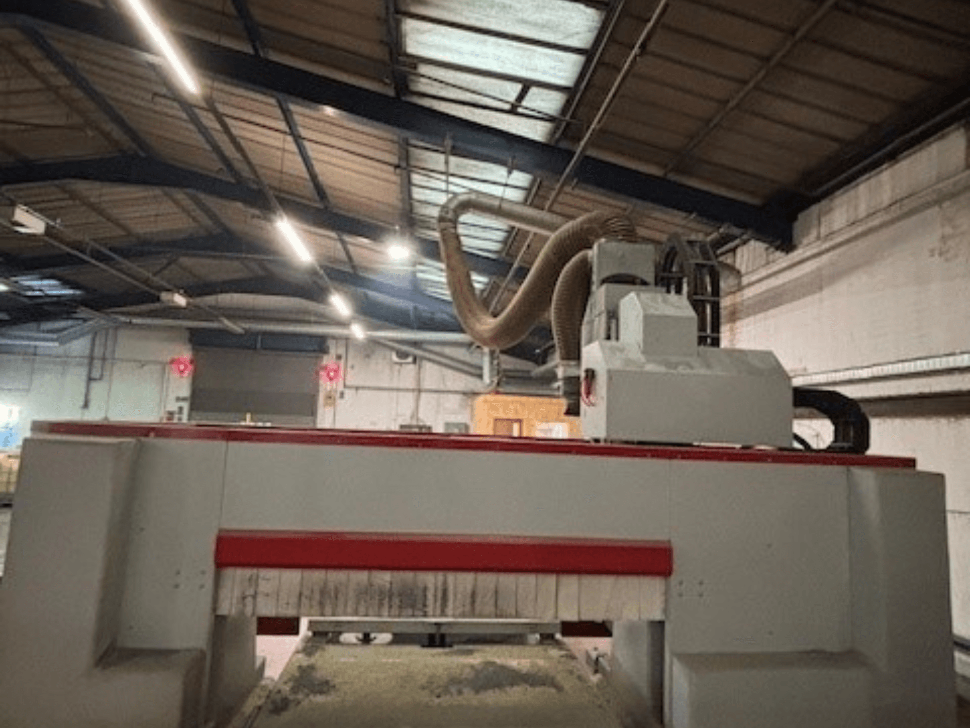 CNC frēzmašīna darbnīcā, skats no sāniem, izceļot sarkano un pelēko dizainu, pievienota putekļu nosūces sistēma.