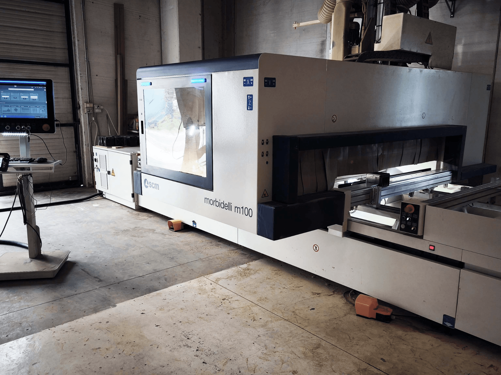 SCM Morbidelli M 100 CNC koka apstrādes centrs no sāniem, kurā redzams vadības panelis, darba zona un drošības elementi.