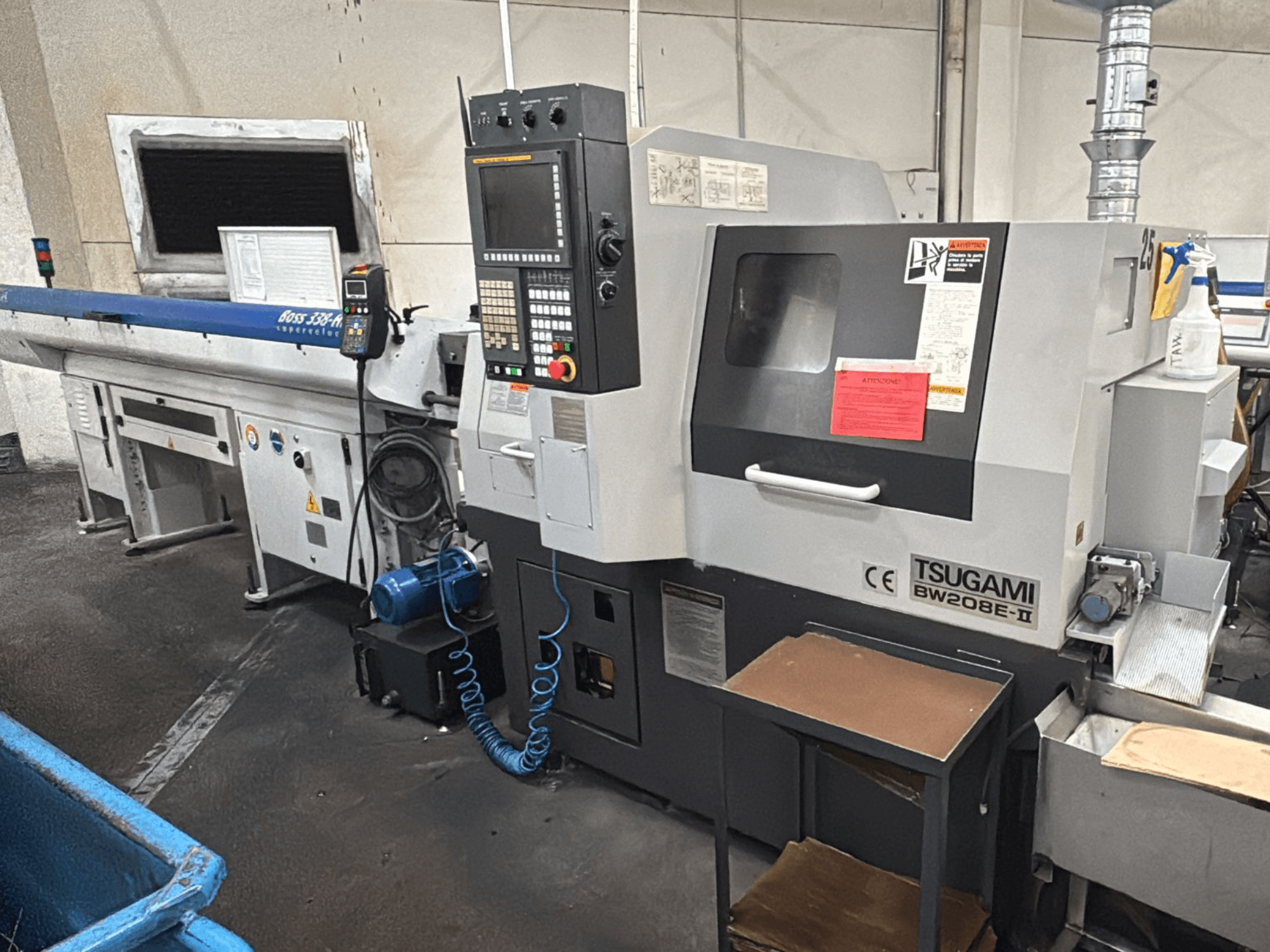 Tsugami BW208E-II CNC mašīna darbnīcā, parādīta no priekšējā leņķa, redzams vadības panelis un drošības marķējums.