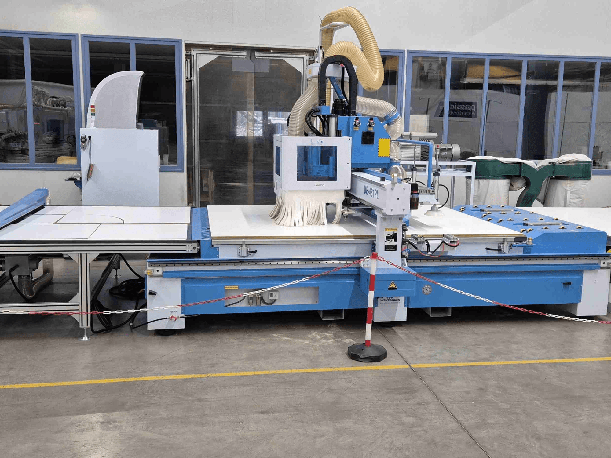 Zilais CNC frēzētājs UE-621PL no priekšpuses, ar lielu griešanas galdu un pievienotu putekļu nosūces sistēmu.