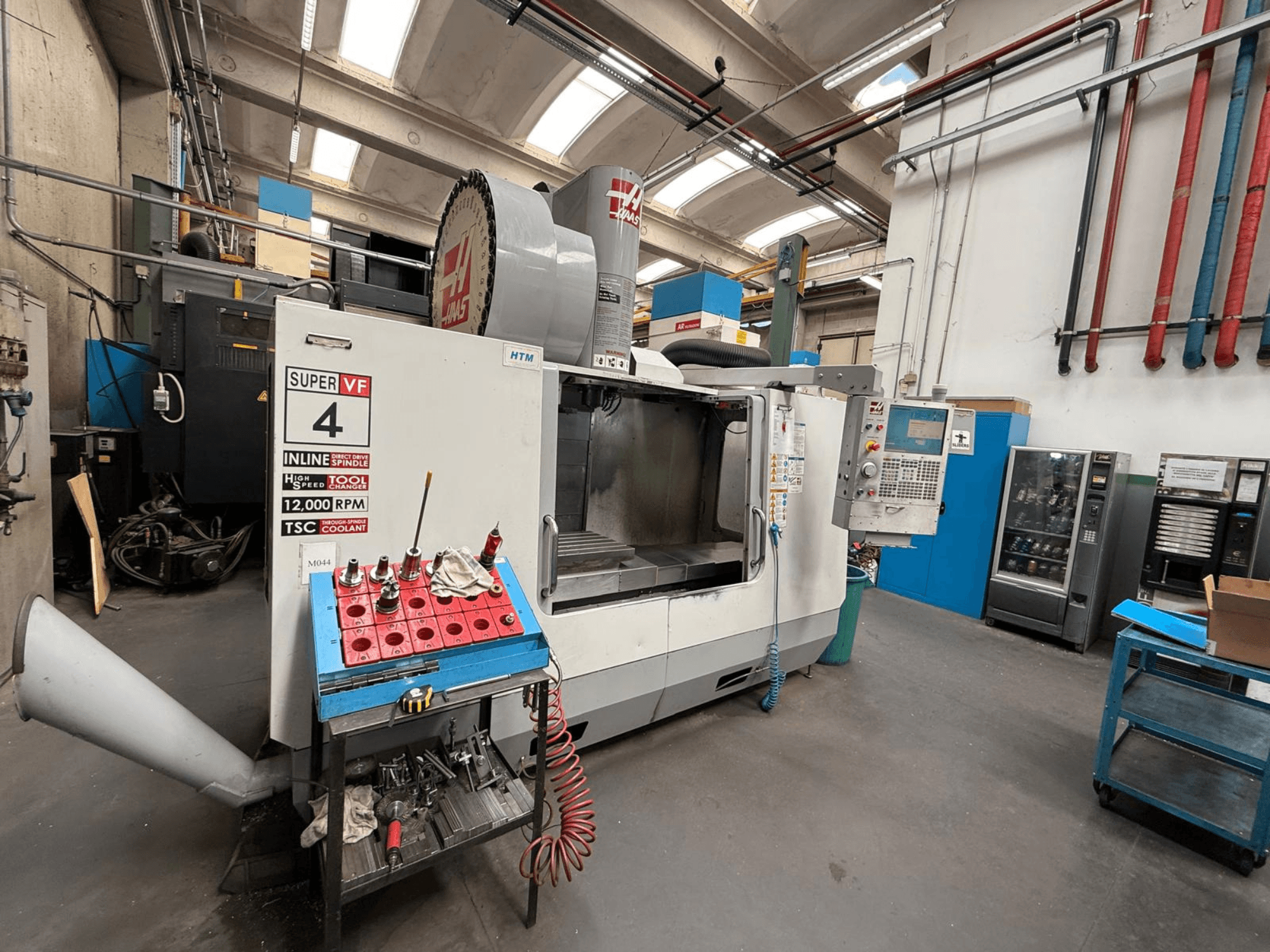 HAAS Super VF 4 CNC frēzmašīna ar vadības paneli, 12 000 apgriezienu/min vārpstu un instrumentiem uz zila glabāšanas statīva, skats no sāniem.