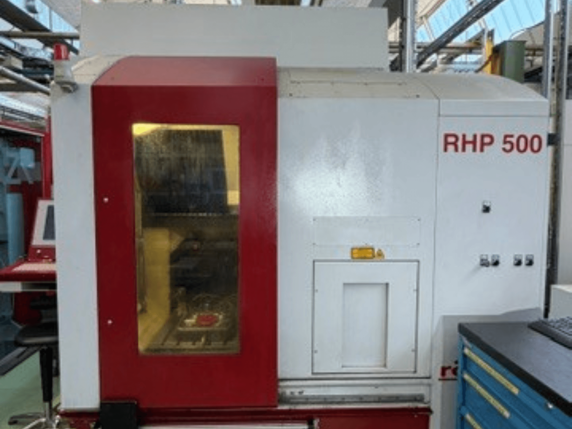 Vertikālais apstrādes centrs „Röders TEC RHP 500“, skats no priekšpuses, kurā redzams vadības panelis un caurspīdīgs logs, kas ļauj ielūkoties iekārtas iekšienē.