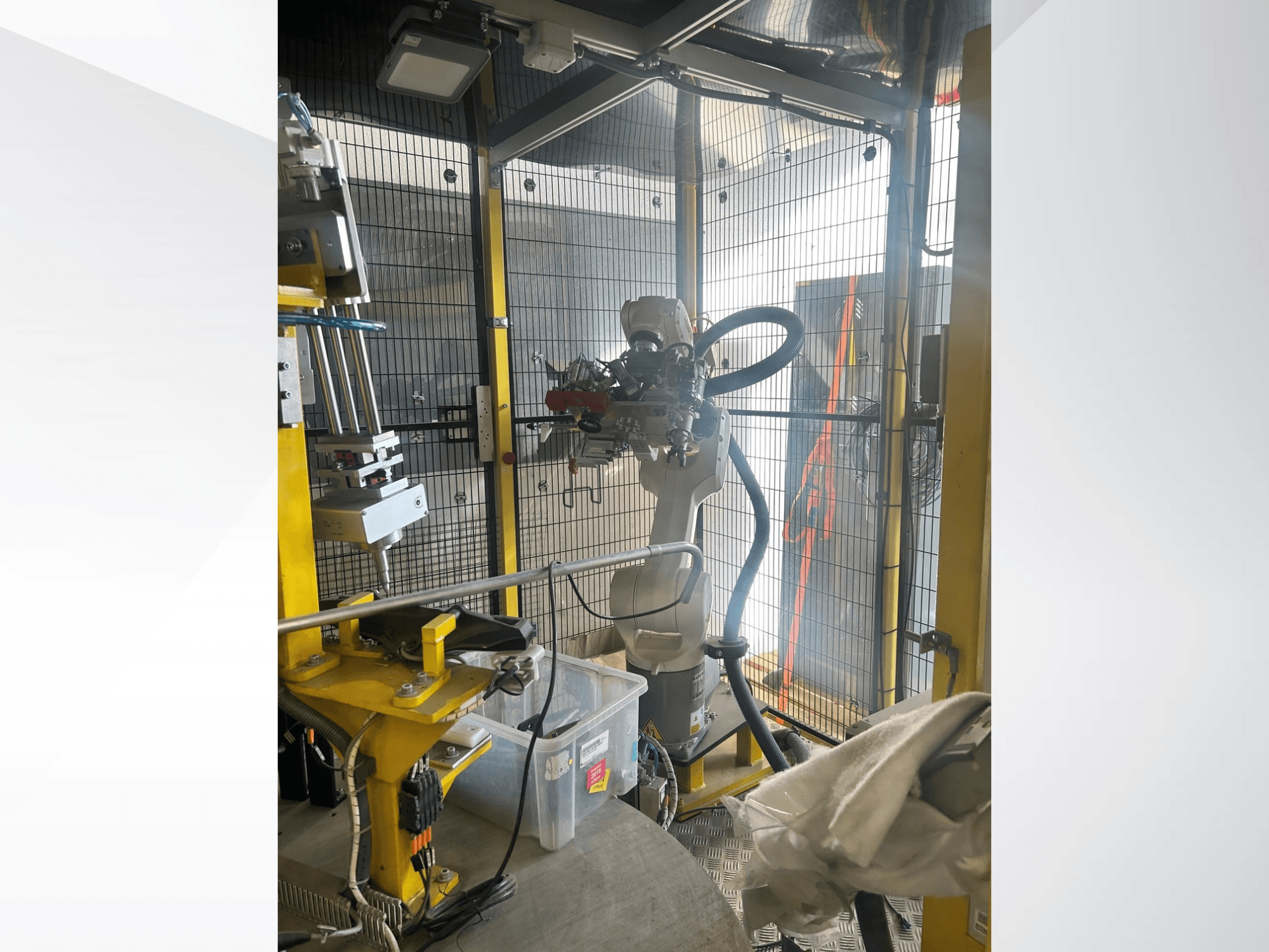 MEI Automotive Automation System robota roka drošā korpusā, skats no priekšpuses, kurā redzamas mehāniskās detaļas un vadības elementi.