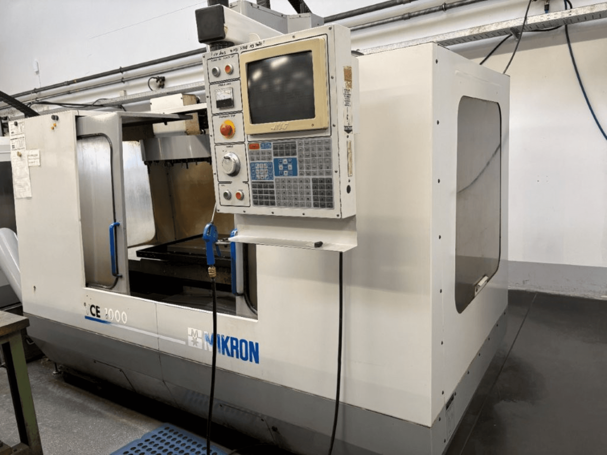 Mikron CE 2000 CNC darbagalds, skats no priekšpuses; vadības panelis ar pogām un ekrānu, sudraba ārpuse un darba zona.