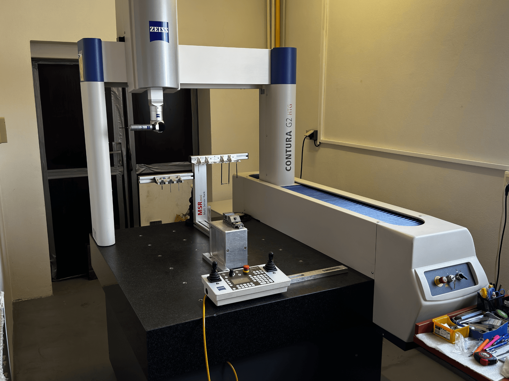 ZEISS Contura G2 CMM laboratorijas apstākļos, priekšējais skats, kurā redzama mērīšanas roka, vadības panelis un blakus esošā darba vieta.