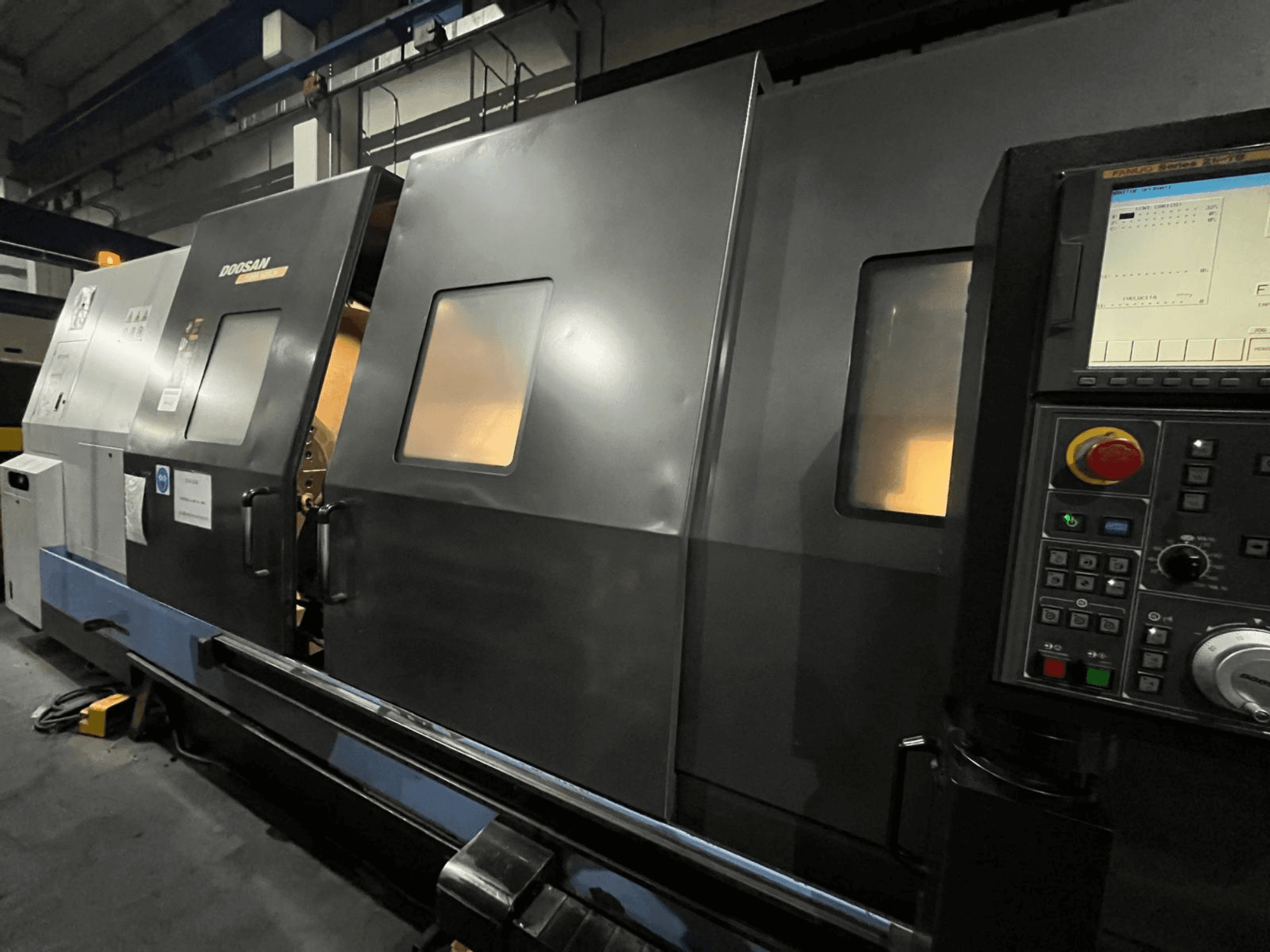 Doosan CNC virpmašīna priekšpusē ar vadības paneli un operatora saskarni ar redzamu digitālo displeju un pogām.