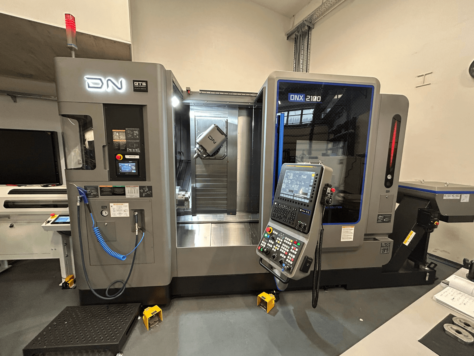 DN ONX 2100 CNC mašīna, skats no priekšpuses, vadības panelis, darba zona un instruments. Aprīkots ar drošības gaismu un darbības indikatoriem.