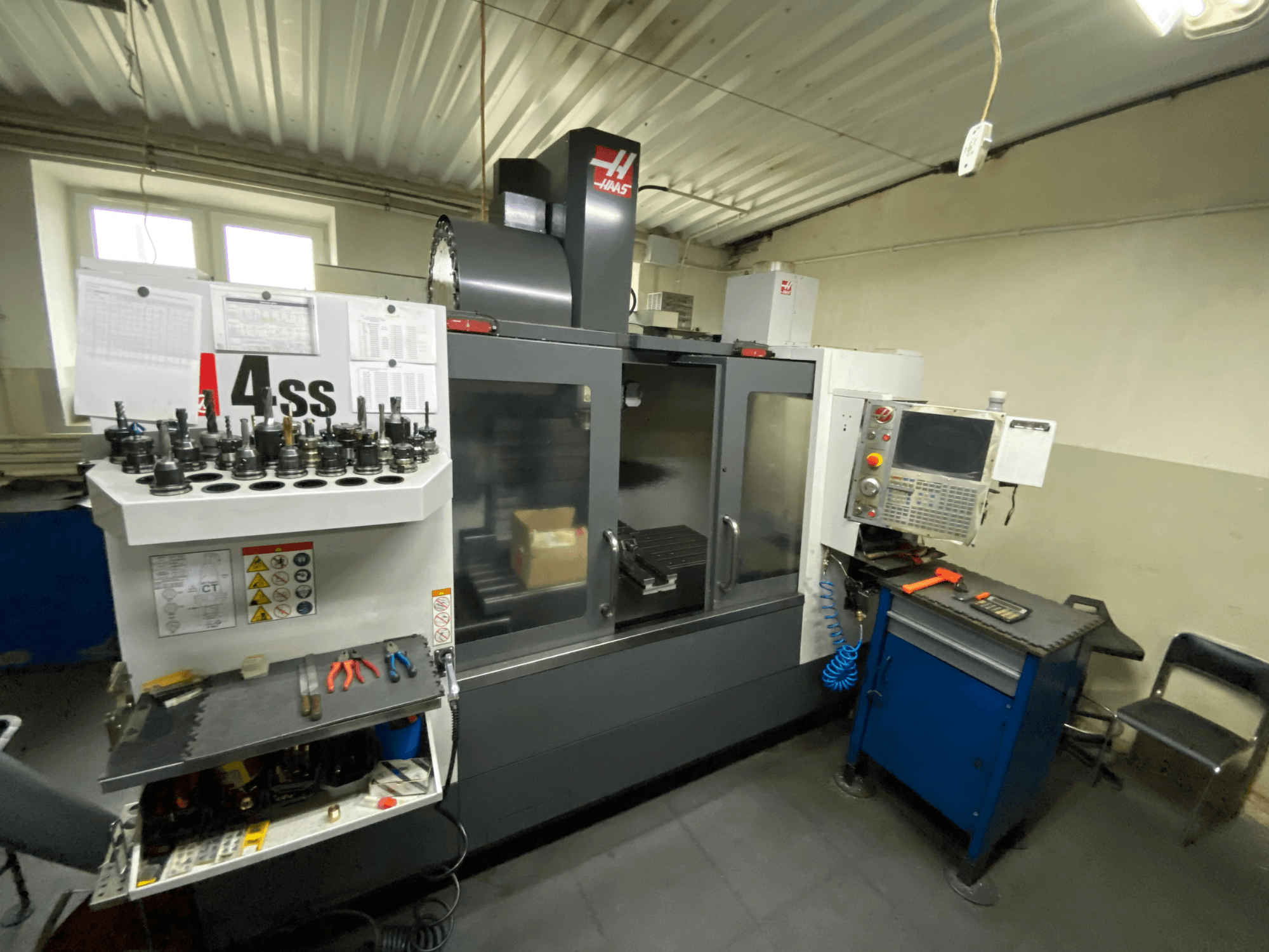 Vertikālais apstrādes centrs Haas VF-4SS, skats no priekšpuses ar instrumentu turētājiem un vadības paneli. Redzami izmantotie instrumenti un darba laukums.
