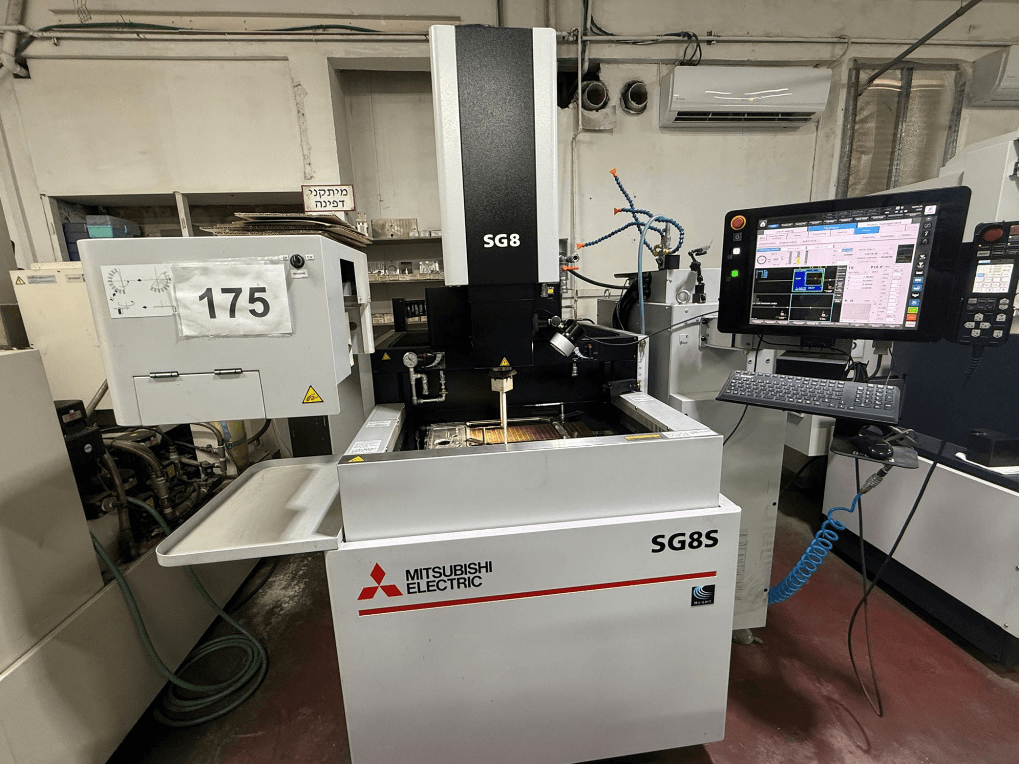 Mitsubishi SG8S štancēšanas EDM mašīna, skats no priekšpuses, redzams monitors un vadības panelis; darba zonā redzams instrumentu iestatījums.