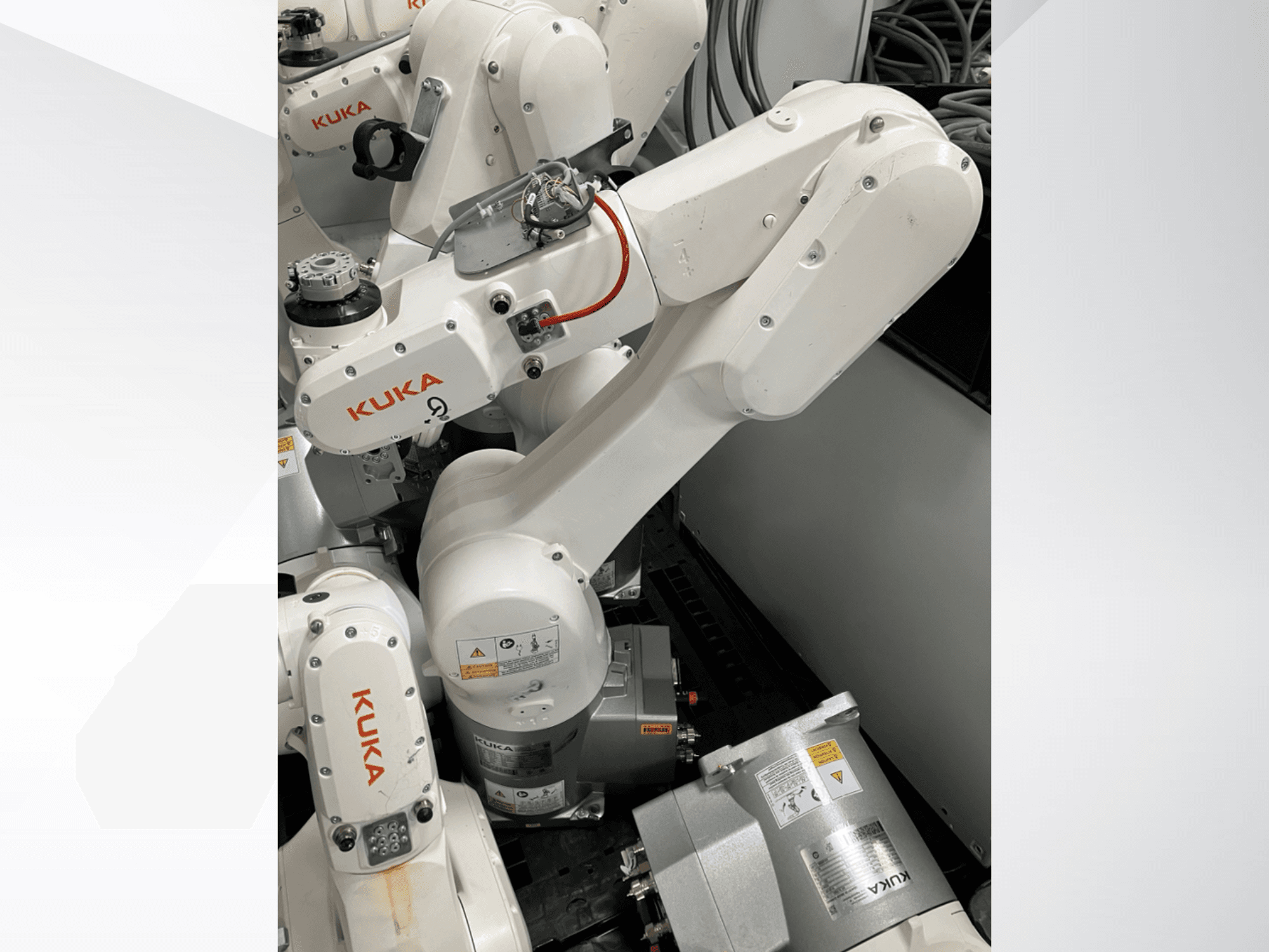 KUKA KR 6 R900 CR robota roka, skats no sāniem; redzami motori un savienotāji, marķēti drošības brīdinājumi un mehāniskās rokas.