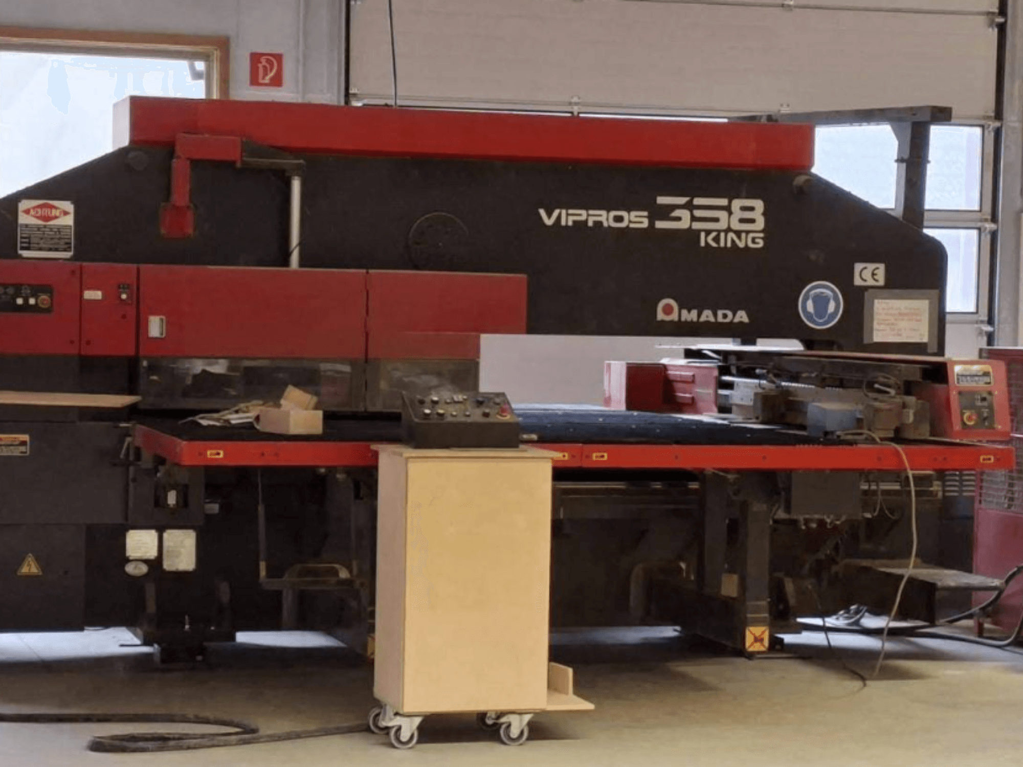 CNC perforācijas preses „AMADA VIPROS 358 KING“ sānskats, kurā redzams vadības panelis un instrumentu uzglabāšanas zona.