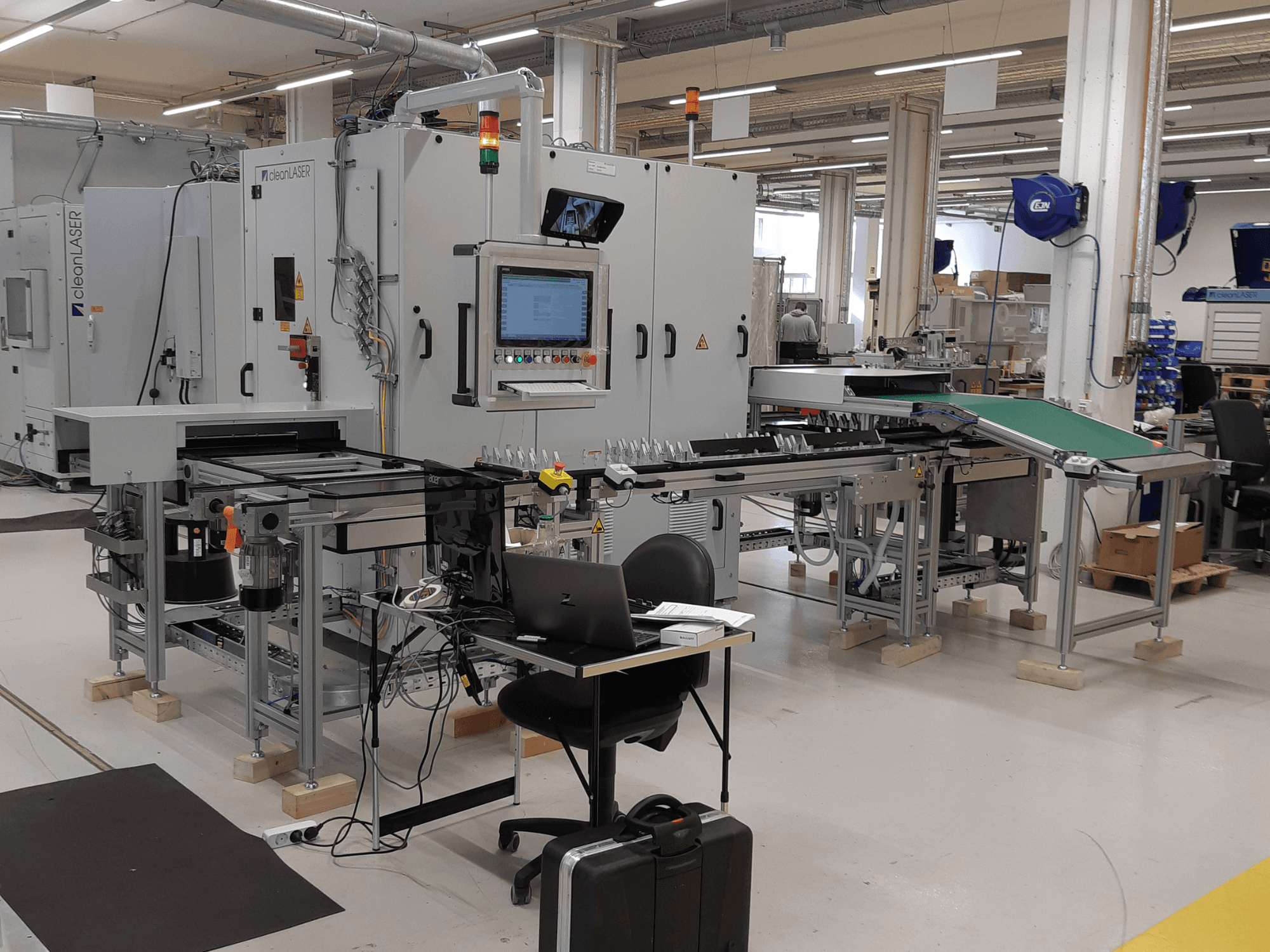 CLEAN LASER „clean CELL 3220” darbgalda priekšskats, kurā redzams vadības panelis, konveijers un darba zonas izkārtojums rūpnīcas vidē.