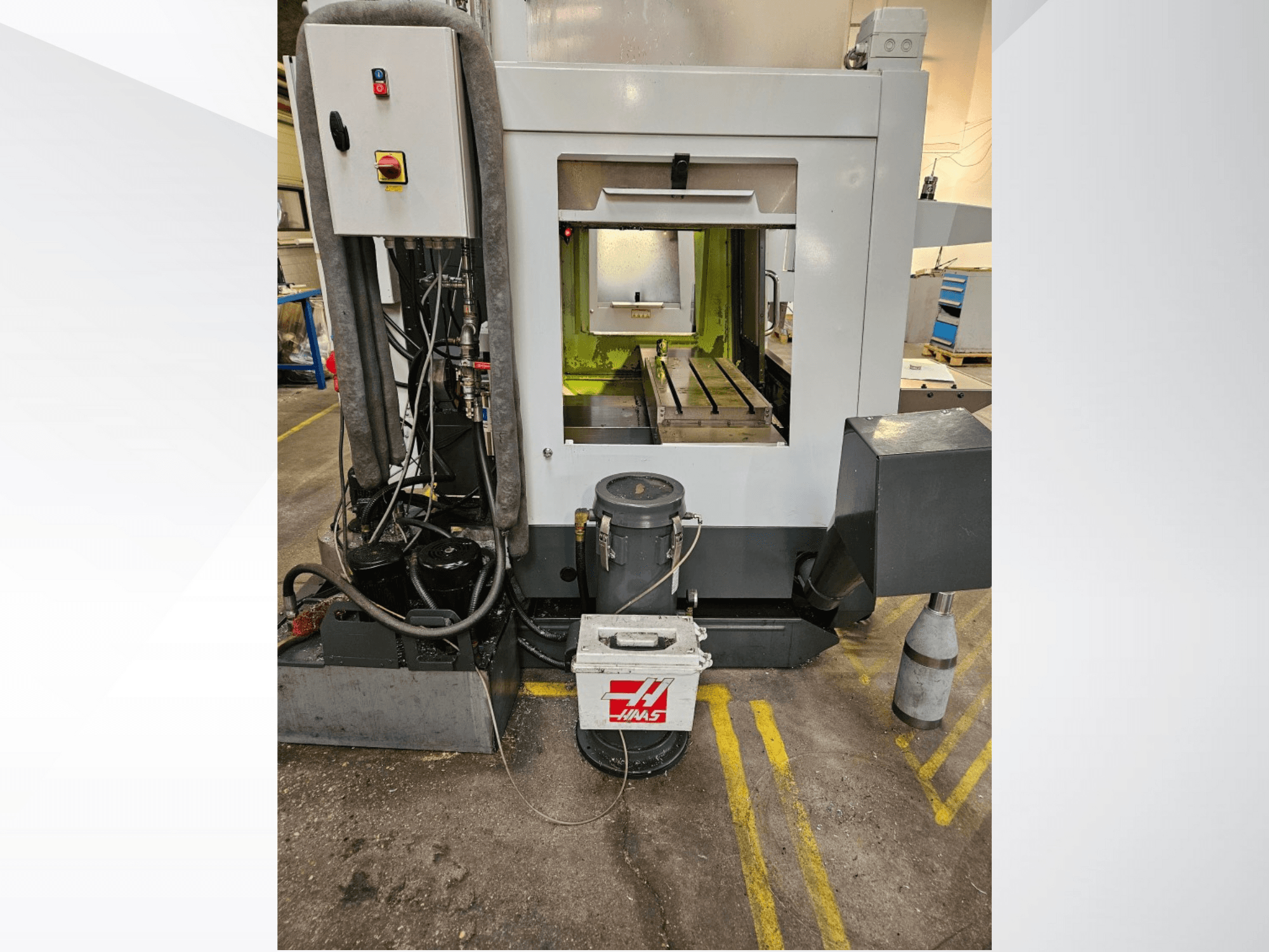 Haas CNC mašīnas priekšējais skats, kurā redzams vadības panelis, dzesēšanas šķidruma tvertne un apstrādātā gultne.