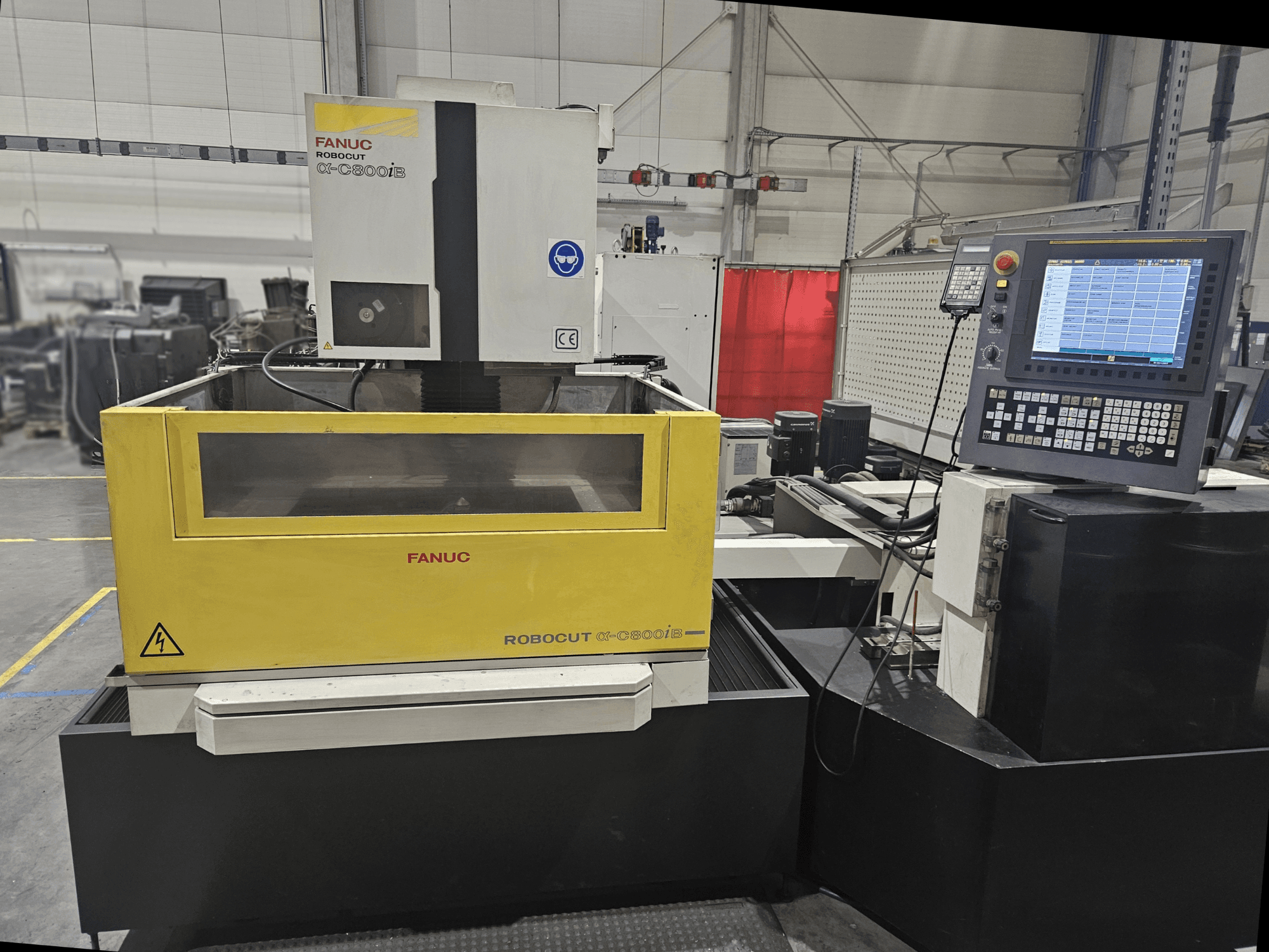 FANUC Robocut α-C600iB priekšējais skats ar dzelteni pelēku mašīnas korpusu, CNC vadības paneli un darbības displeju.