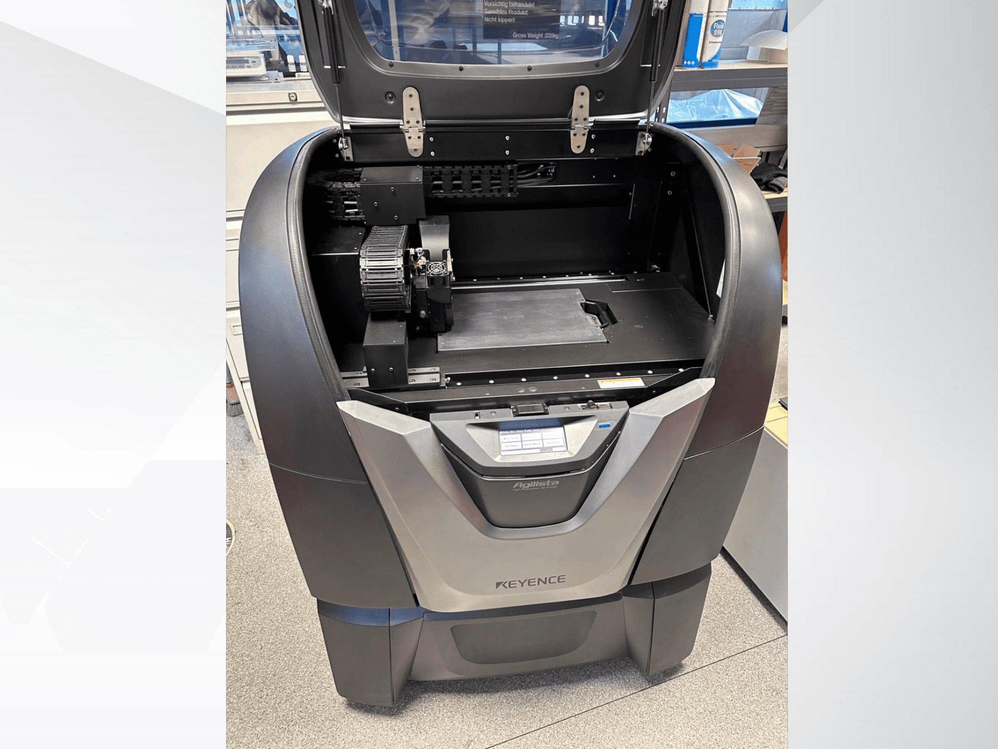 KEYENCE Agilista 3D printeris, skats no priekšpuses, atklāj atvērtu augšējo daļu, lielu veidošanas platformu un iekšējās mehāniskās sastāvdaļas.