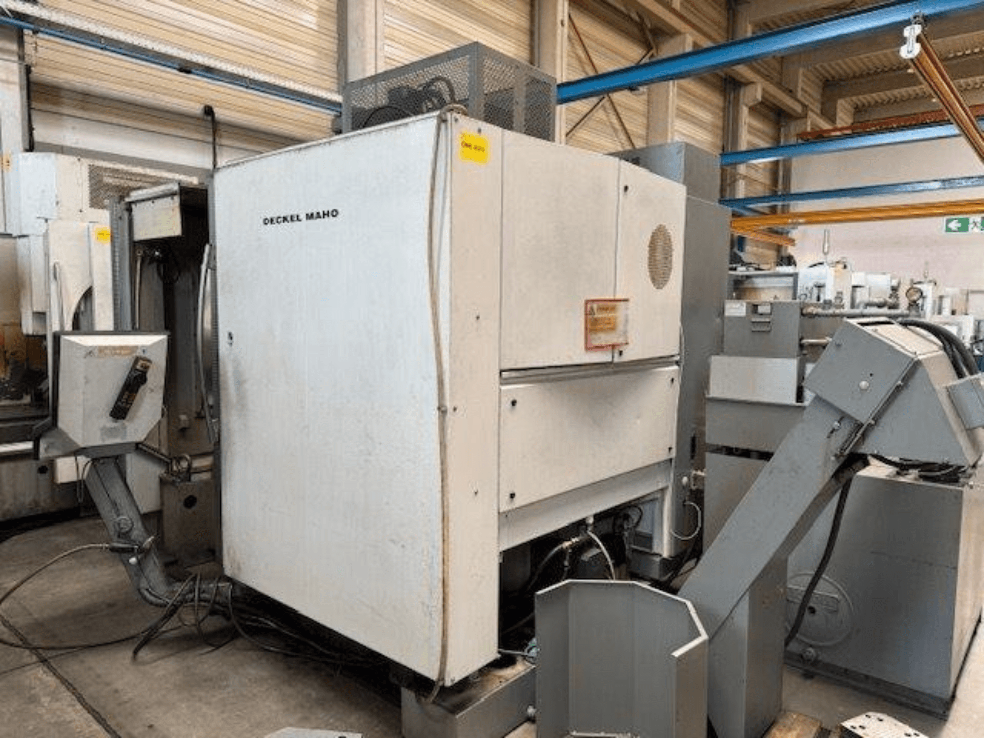DECKEL MAHO DMC 100 V vertikālais apstrādes centrs, skats no sāniem, redzams vadības panelis un dažādi stiprinājumi.