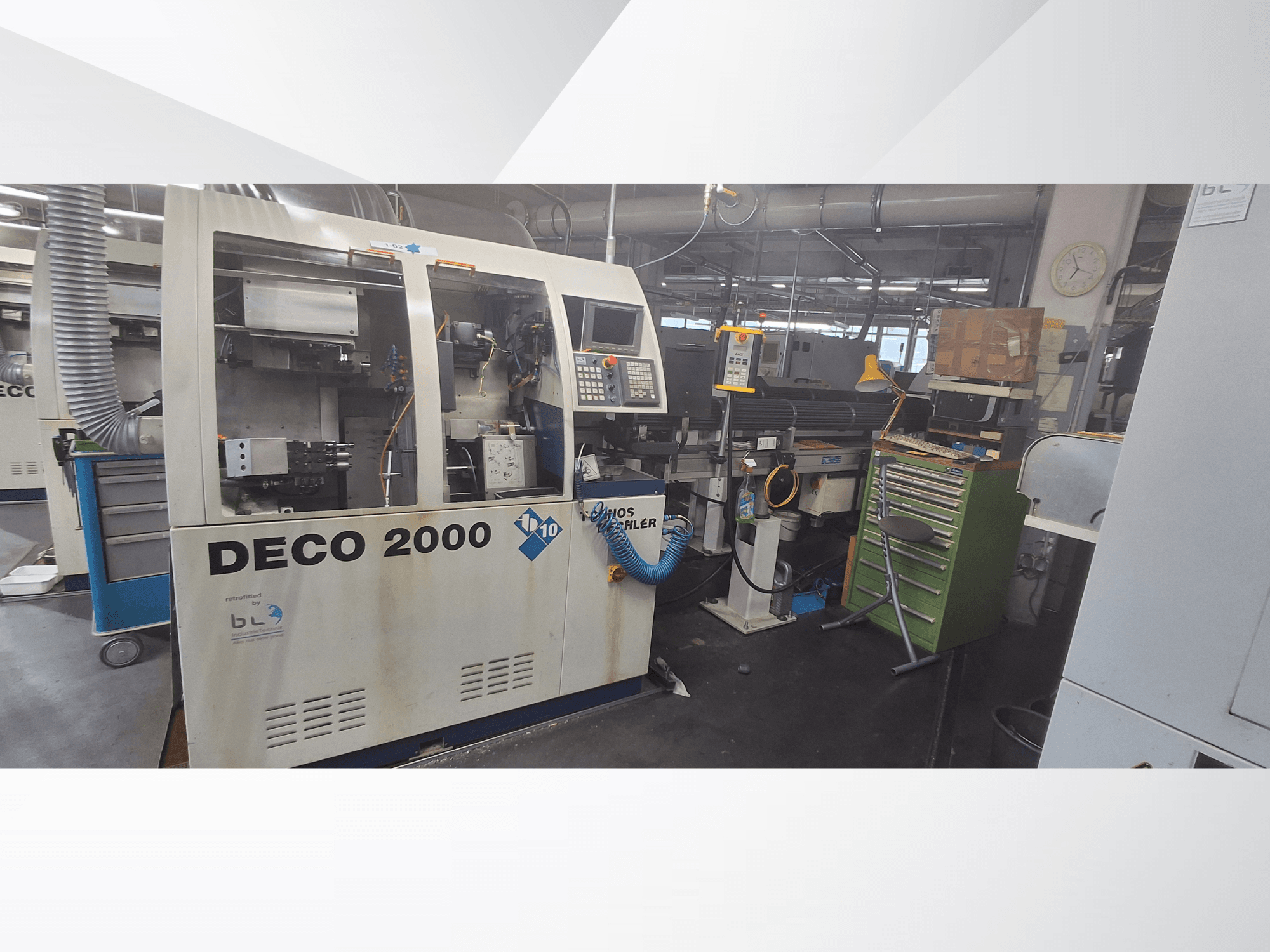 Šveices tipa virpošanas stends TORNOS DECO 2000-10, skats no priekšpuses, kurā redzams vadības panelis un iekraušanas zona darbnīcas vidē.