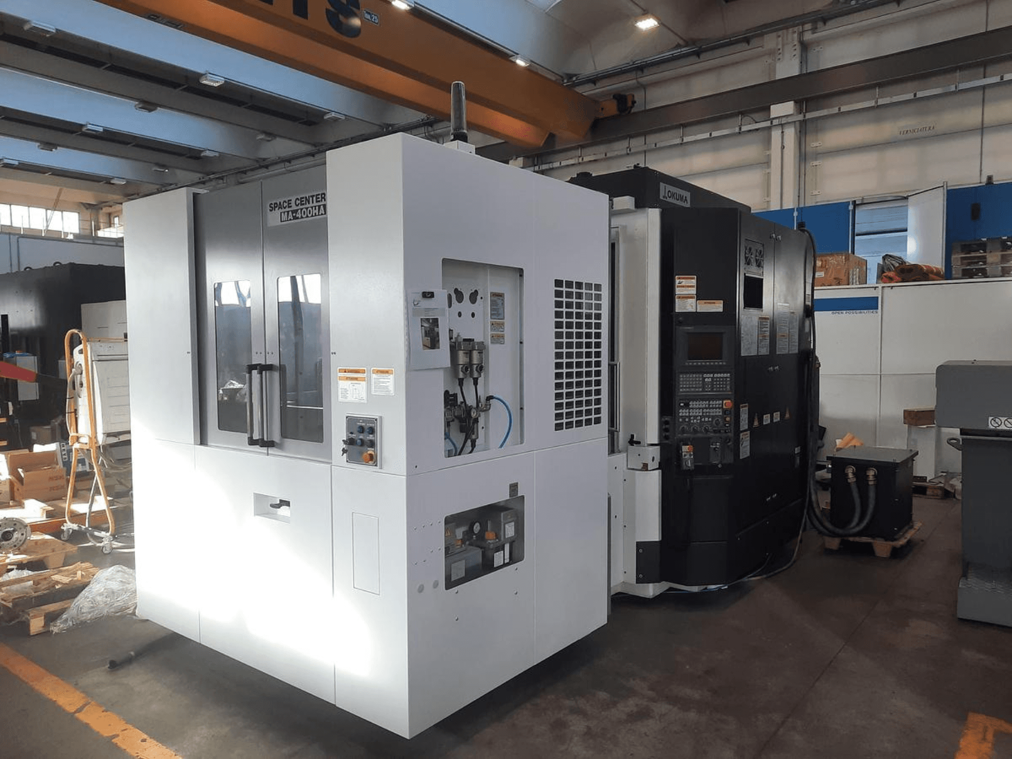 SPACE CENTER IM-400HAA un OKUMA CNC mašīnu priekšējais skats, kurā redzamas dažādas vadības ierīces un ražotāja uzlīmes.