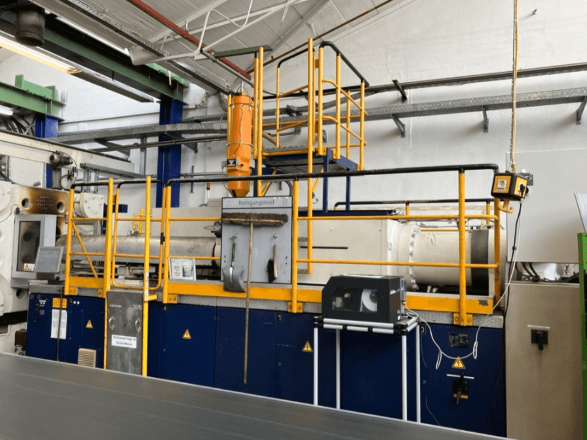 Krauss Maffei 1000-8000 M hidrauliskā iesmidzināšanas iekārta, skats no sāniem, redzamas drošības margas un vadības panelis.