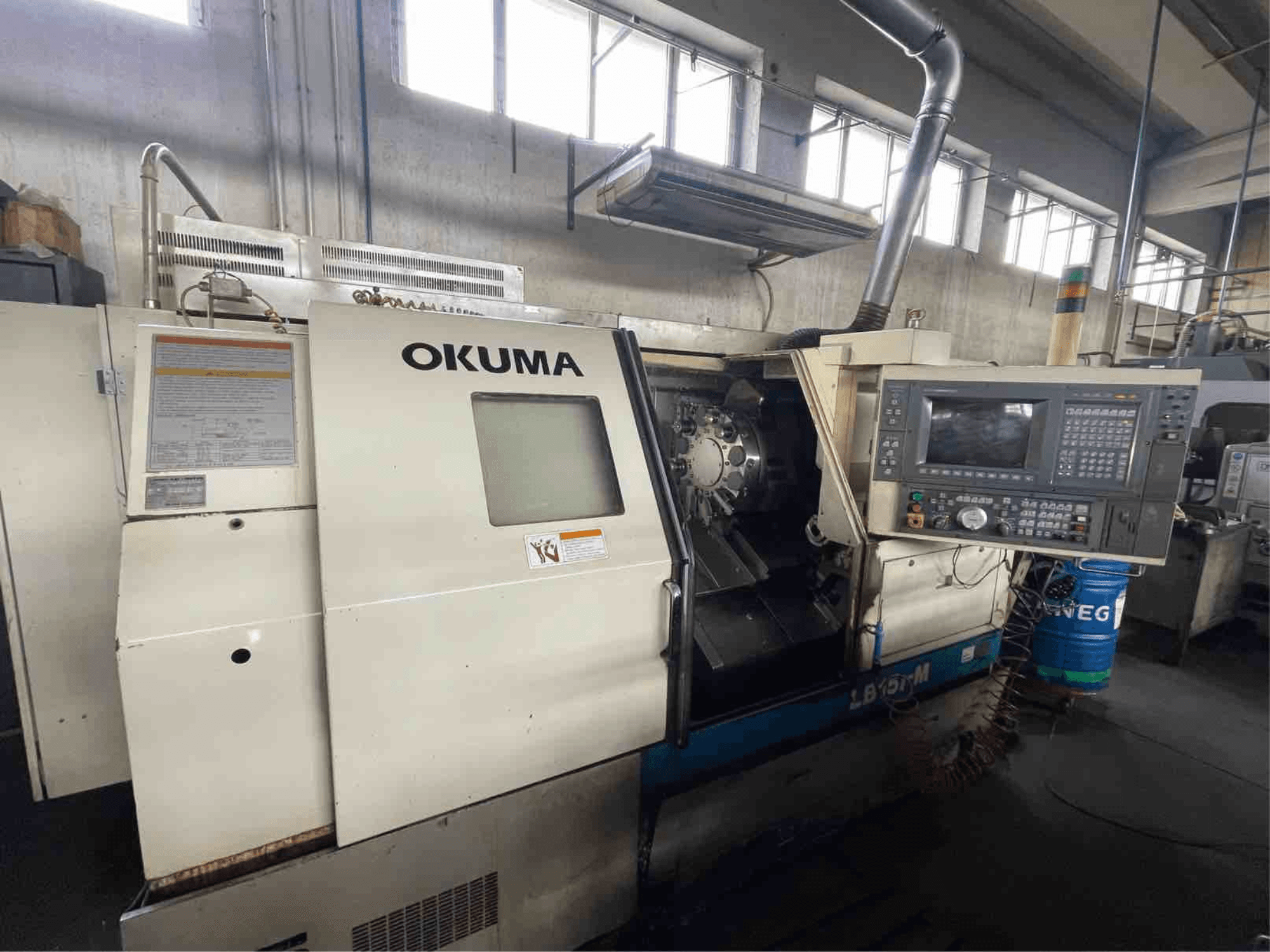 Okuma LB15i-M horizontālās virpošanas iekārta, skats no priekšpuses; vadības panelis un griezējinstrumentu zona ar detalizētiem indikatoriem.
