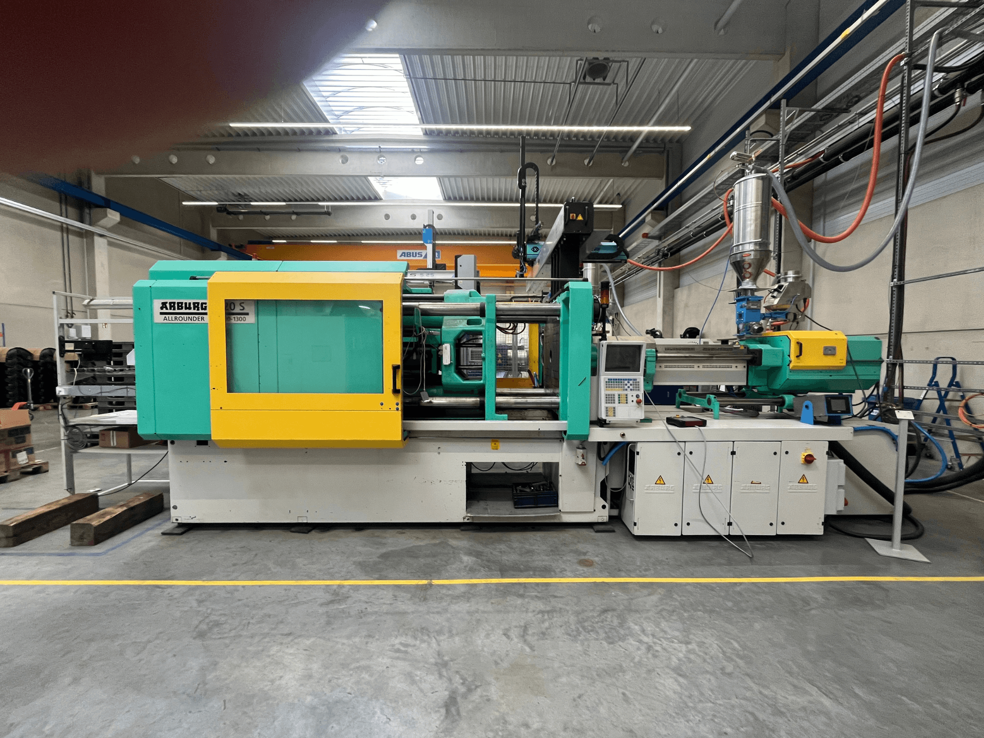 ARBURG Allrounder 370S plastmasas iesmidzināšanas iekārta, skats no sāniem, ar zaļu un dzeltenu korpusu, redzams vadības interfeiss.