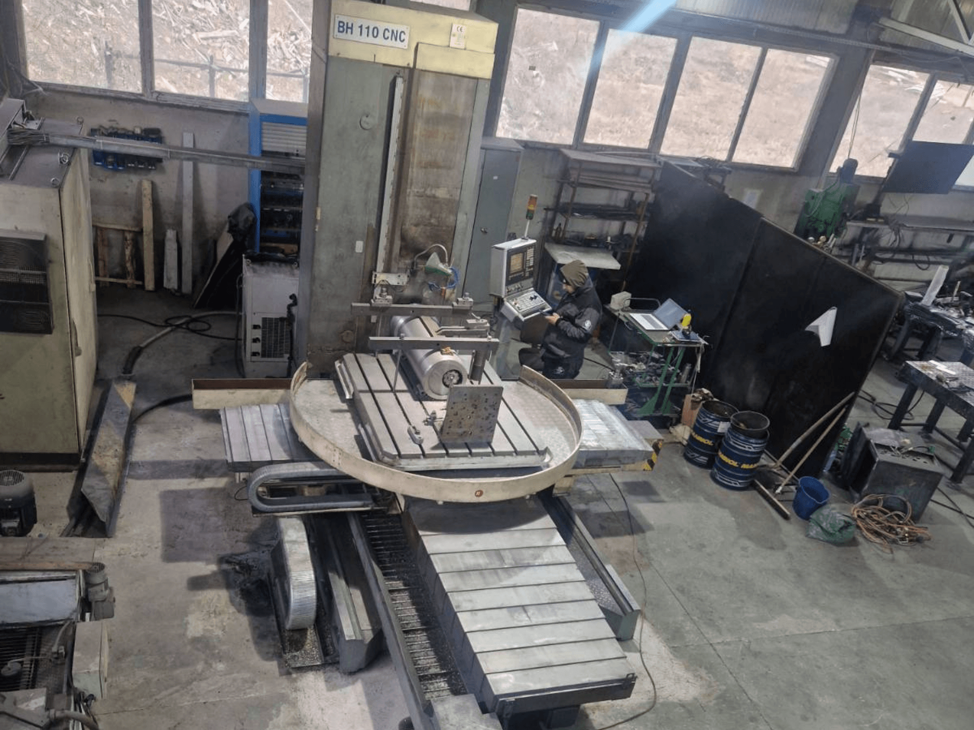LOLA BH 110 CNC urbjmašīna, kas parādīta no augšas, ar apaļo galdu, vadības ierīcēm un sagataves iestatījumu.