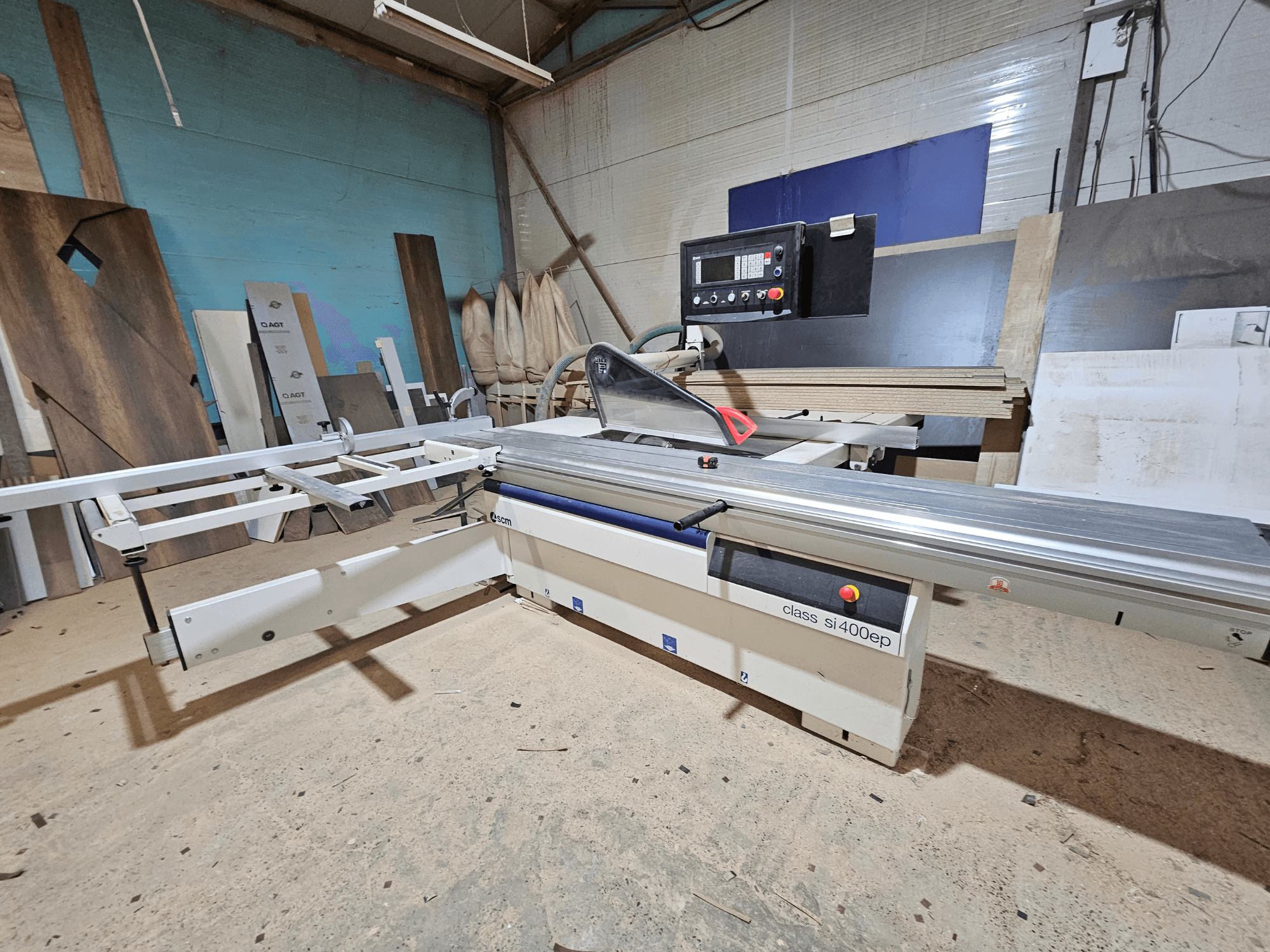 SI400EP klases paneļu zāģis, skats no priekšpuses, ar regulējamu žogu, novietots uz smilšainas darbnīcas grīdas, ieskauj koka paneļi.