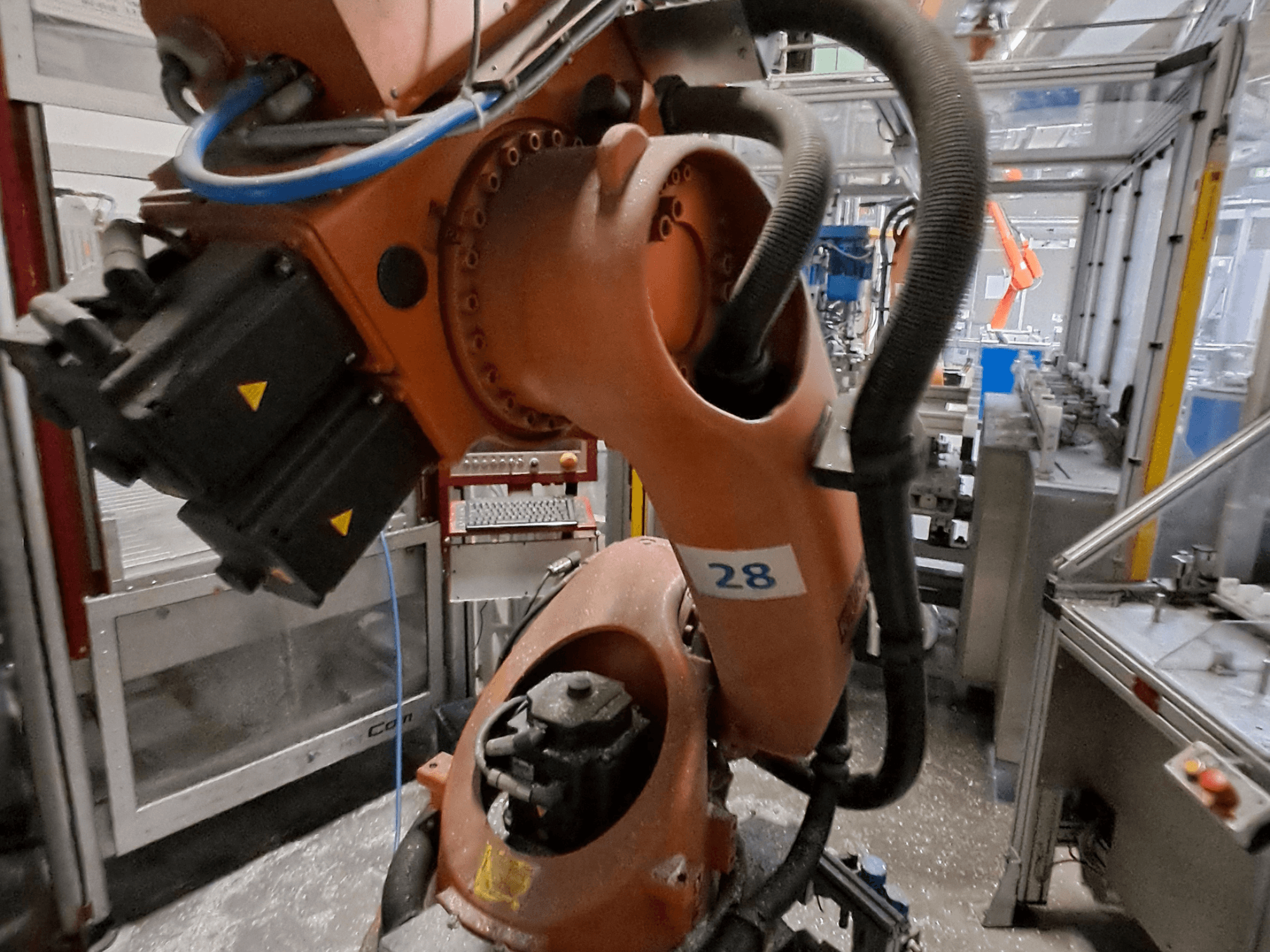 KUKA KR30-3 robota rokas tuvplāns — oranža korpusa, ar numuru 28, kurā no sāniem redzami motori un vadu izvietojums.