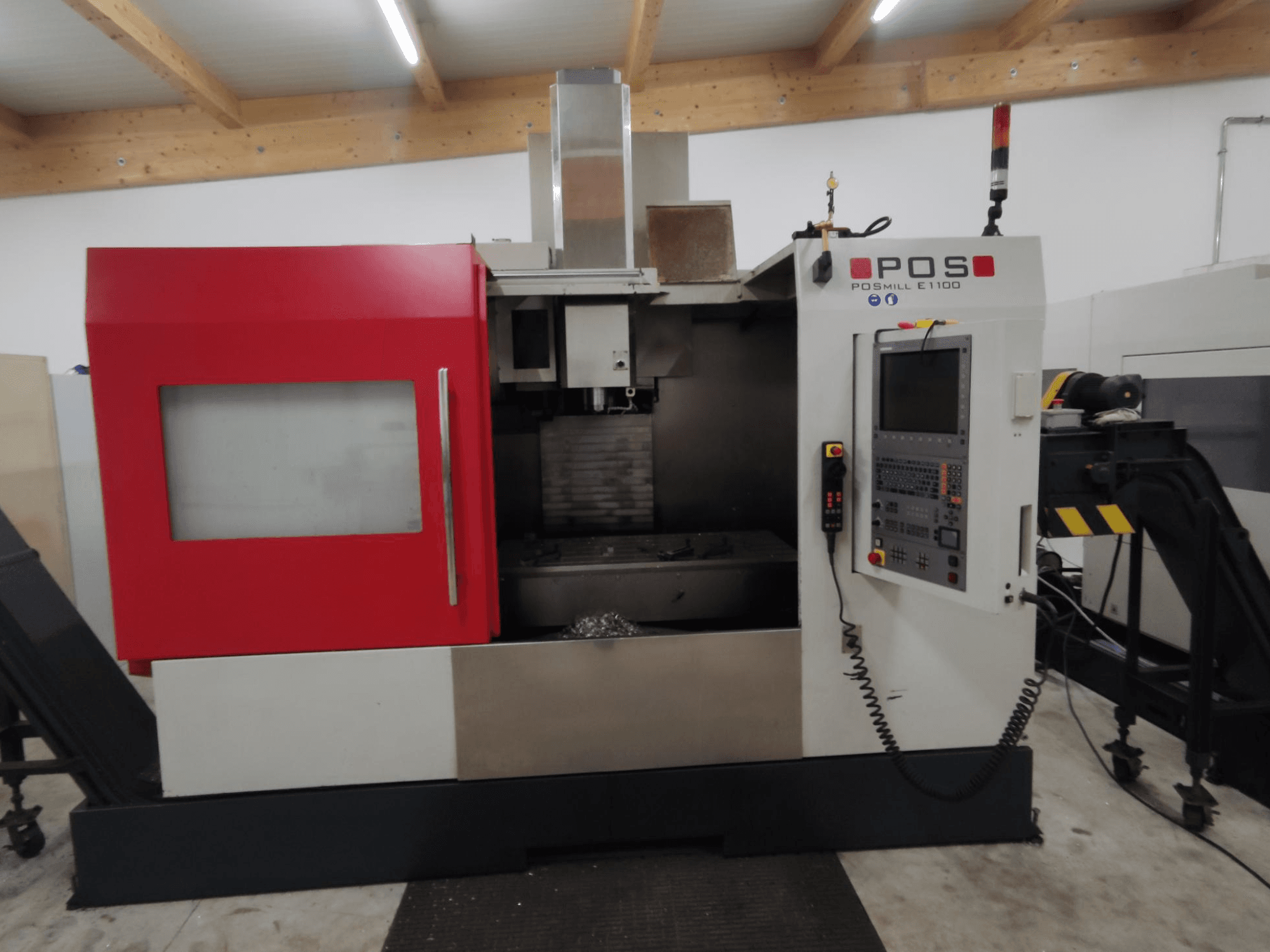 POS POSMILL E1100 CNC frēzmašīna priekšpusē ar sarkanu korpusu, vadības paneli un drošības gaismu augšpusē.