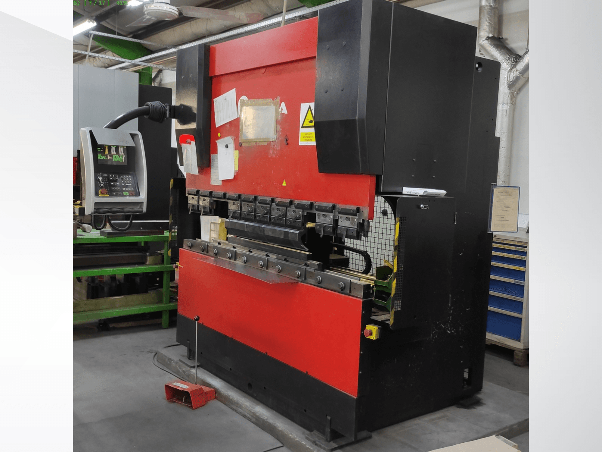 AMADA HFB 5020 preses bremze sarkanā un melnā krāsā, skats no priekšpuses, kurā redzams vadības panelis, lieces instrumenti un drošības elementi.