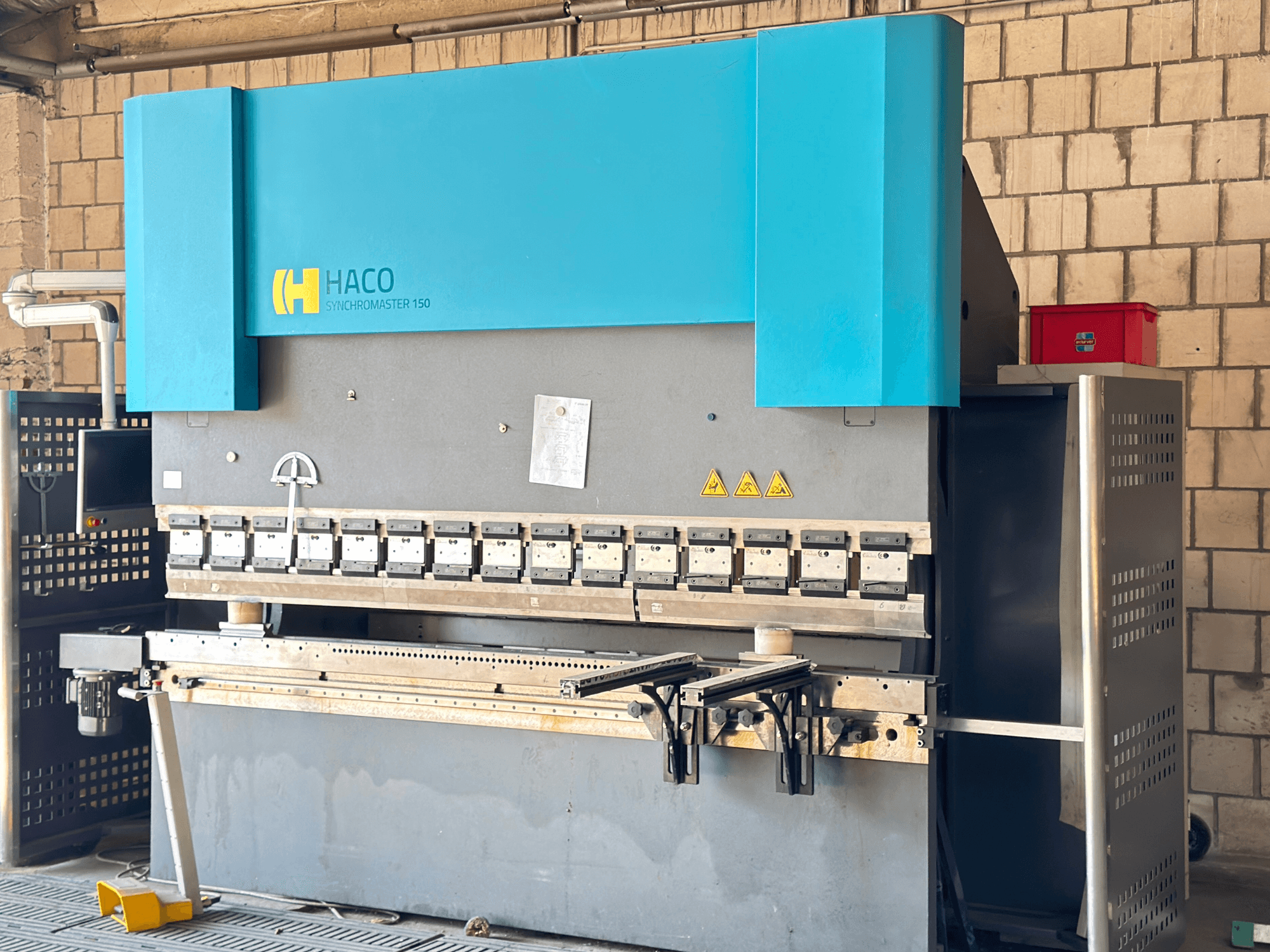 Preses bremze HACO SRM30150, skats no priekšpuses; ietver vadības paneli un iespīlēšanas preses, ar redzamām drošības brīdinājuma uzlīmēm.