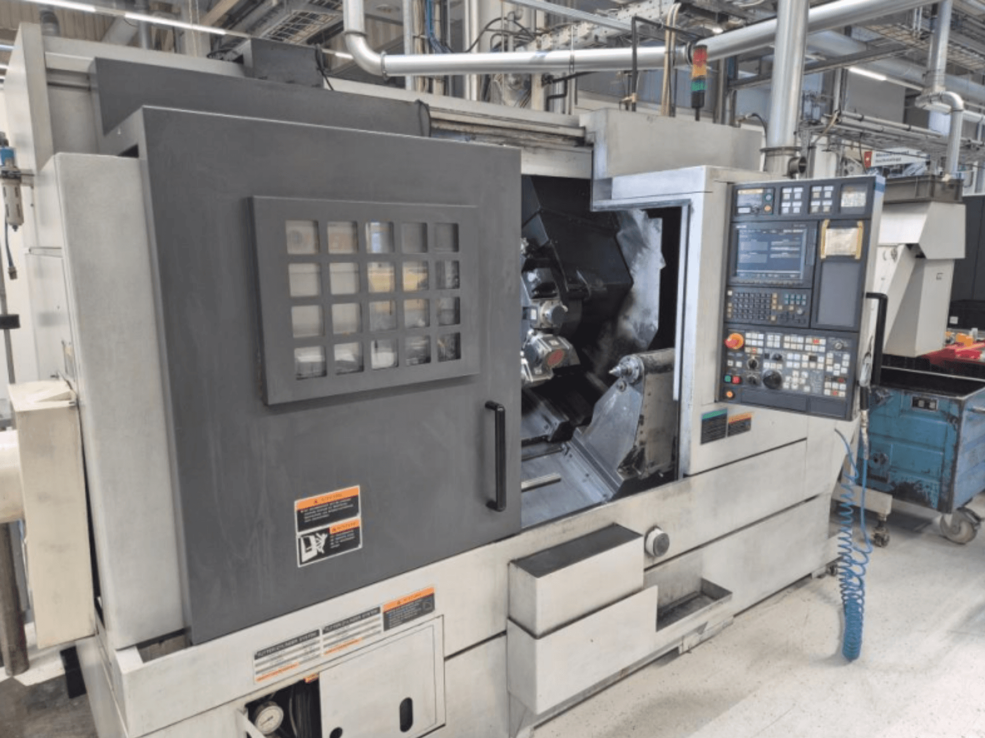 CNC virpmašīna ar vadības paneli, skats no priekšpuses. Ar redzamu darba zonu un drošības logu, zīmols nav zināms.