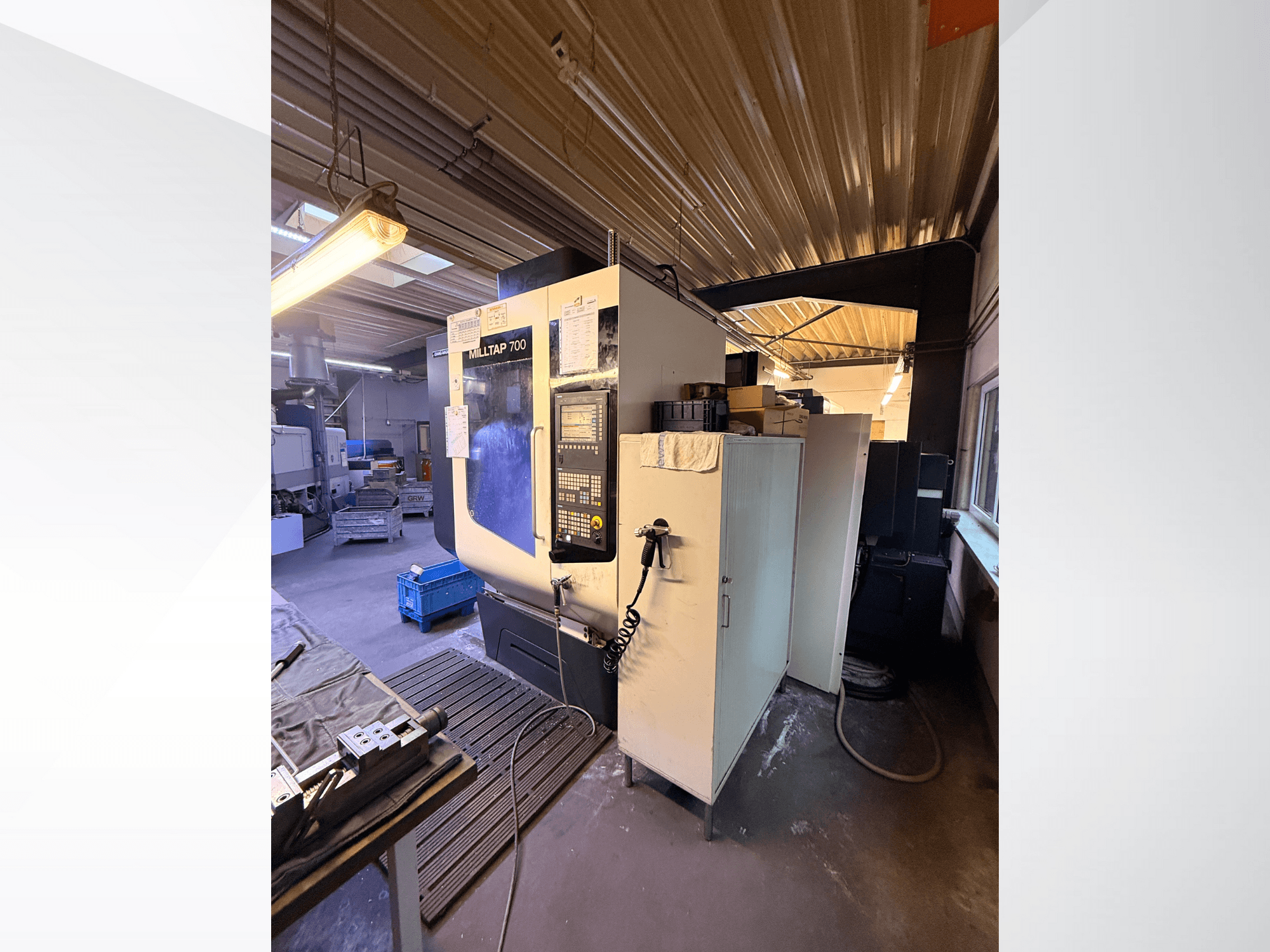 Milltap 700 CNC darbnīcā; priekšpusē redzams vadības panelis, instrumentu plaukti un uzglabāšanas zonas ar apgaismojumu virs tām.