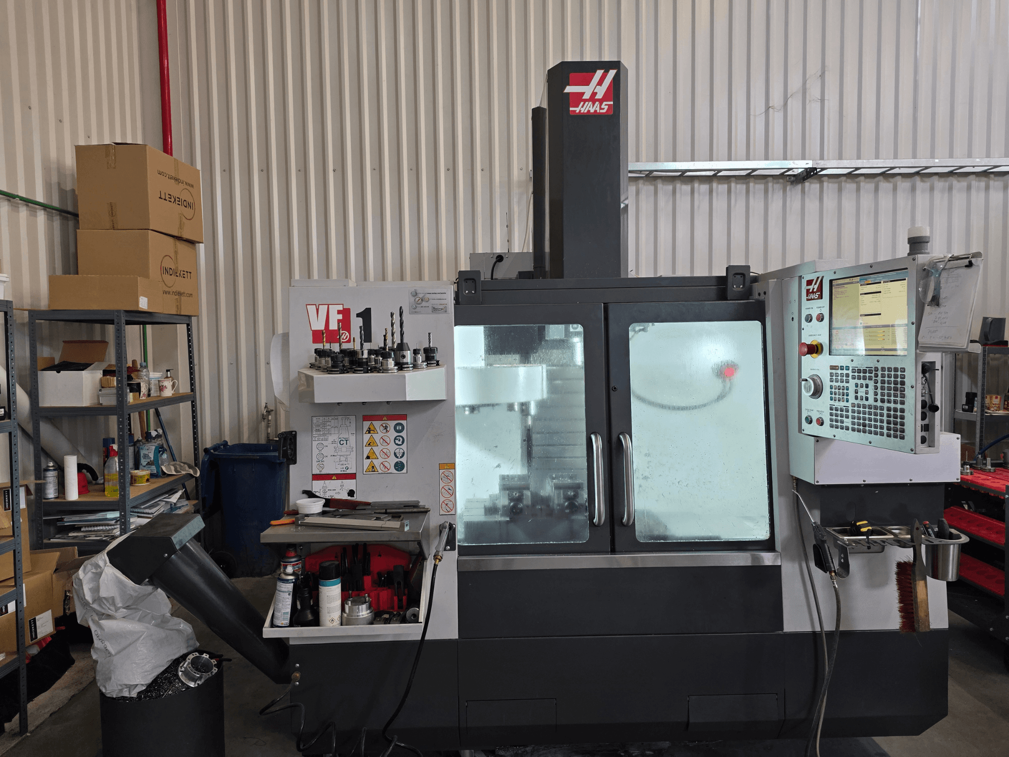 HAAS VF 1 vertikālās apstrādes centrs darbnīcā, priekšējais skats, kurā redzams vadības panelis un frēzēšanas zona ar instrumentiem.