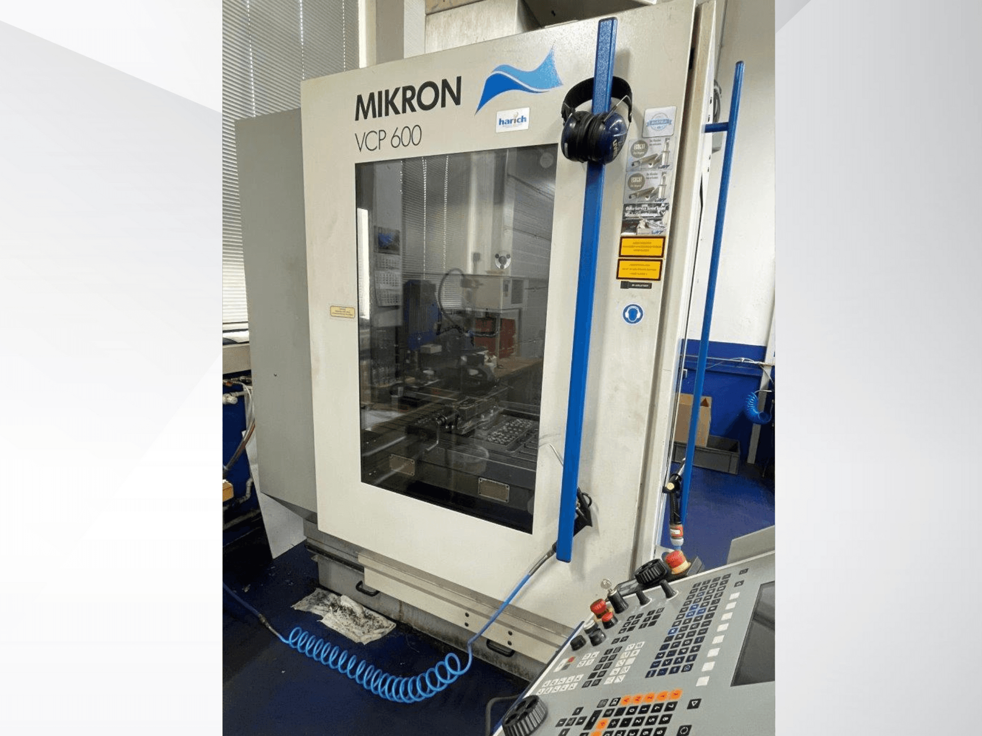 Mikron VCP 600 CNC darbagalds, skats no priekšpuses, vadības panelis ar pogām un redzama apstrādes zona aiz stikla.