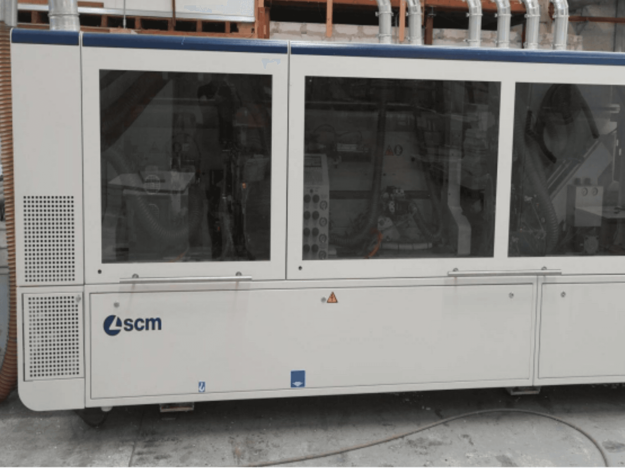 SCM industriālā mašīna, skats no sāniem, ar caurspīdīgiem paneļiem un redzamām ventilācijas atverēm; paredzēta ražošanas procesu efektivitātei.