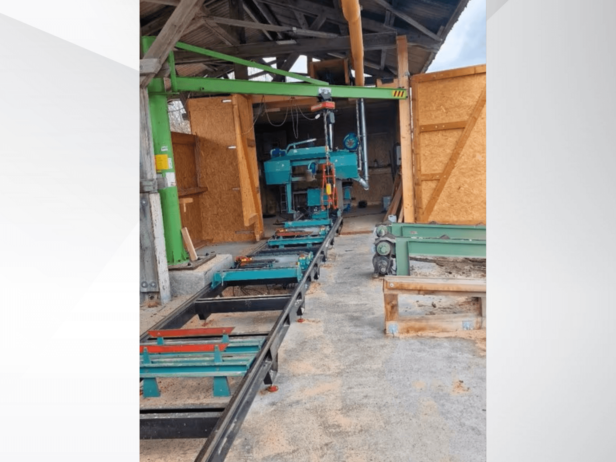 Horizontālais lentzāģis darbnīcā, skatīts no priekšpuses. Aprīkojumā ietilpst sliede un papildu zaļās krāsas piederumi.