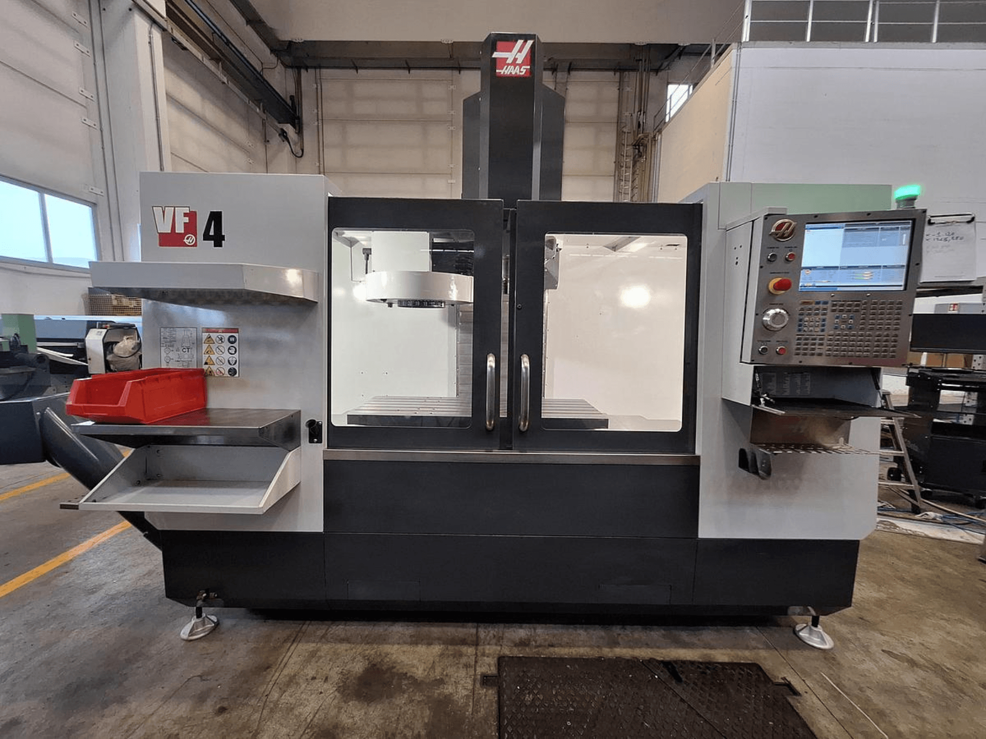 Haas VF-4 vertikālais apstrādes centrs, skats no priekšpuses, ar vadības paneli, instrumentu turētāju un plašu darba zonu.