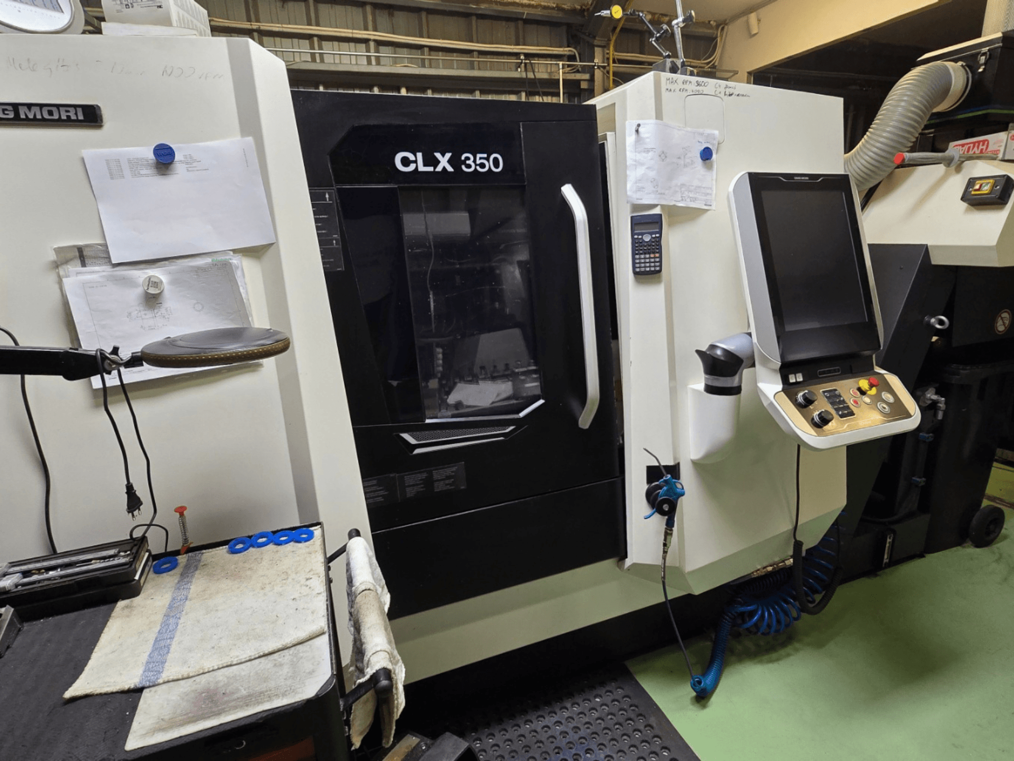 DMG MORI CLX 350 CNC virpa darbnīcā; skats no priekšpuses ar redzamu vadības paneli, instrumentiem un darba vietu.