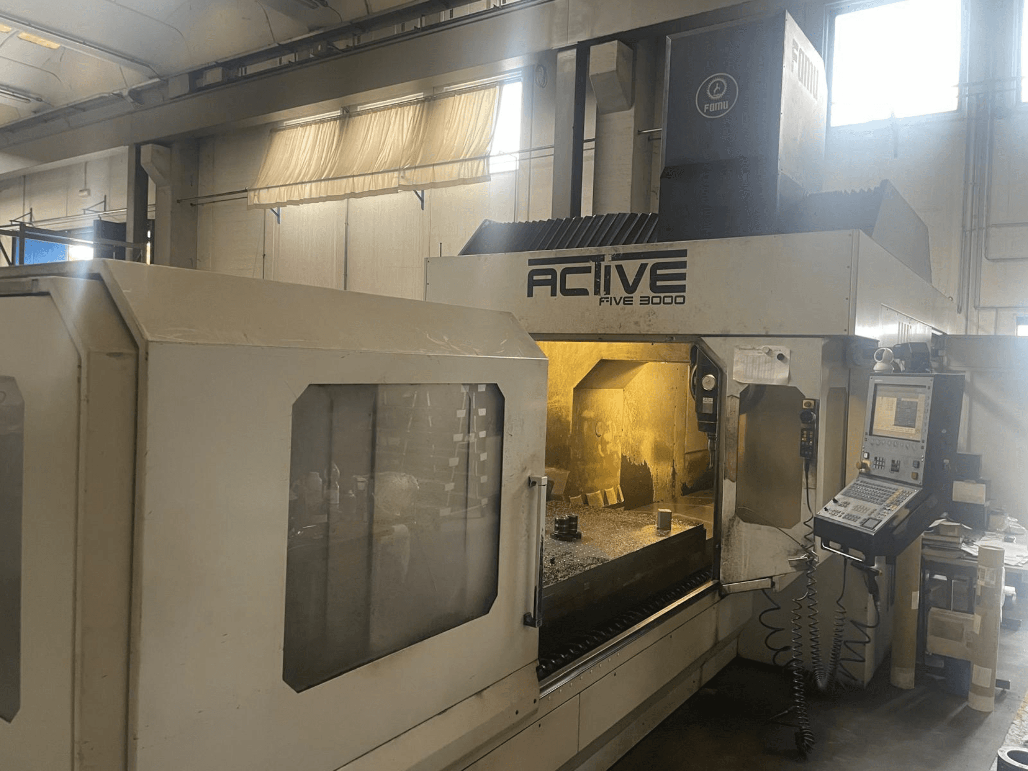 ACTIVE Five 3000 CNC mašīnas priekšējais skats, kurā redzams vadības panelis un darba zona ar daļēji apstrādātu detaļu iekšpusē.
