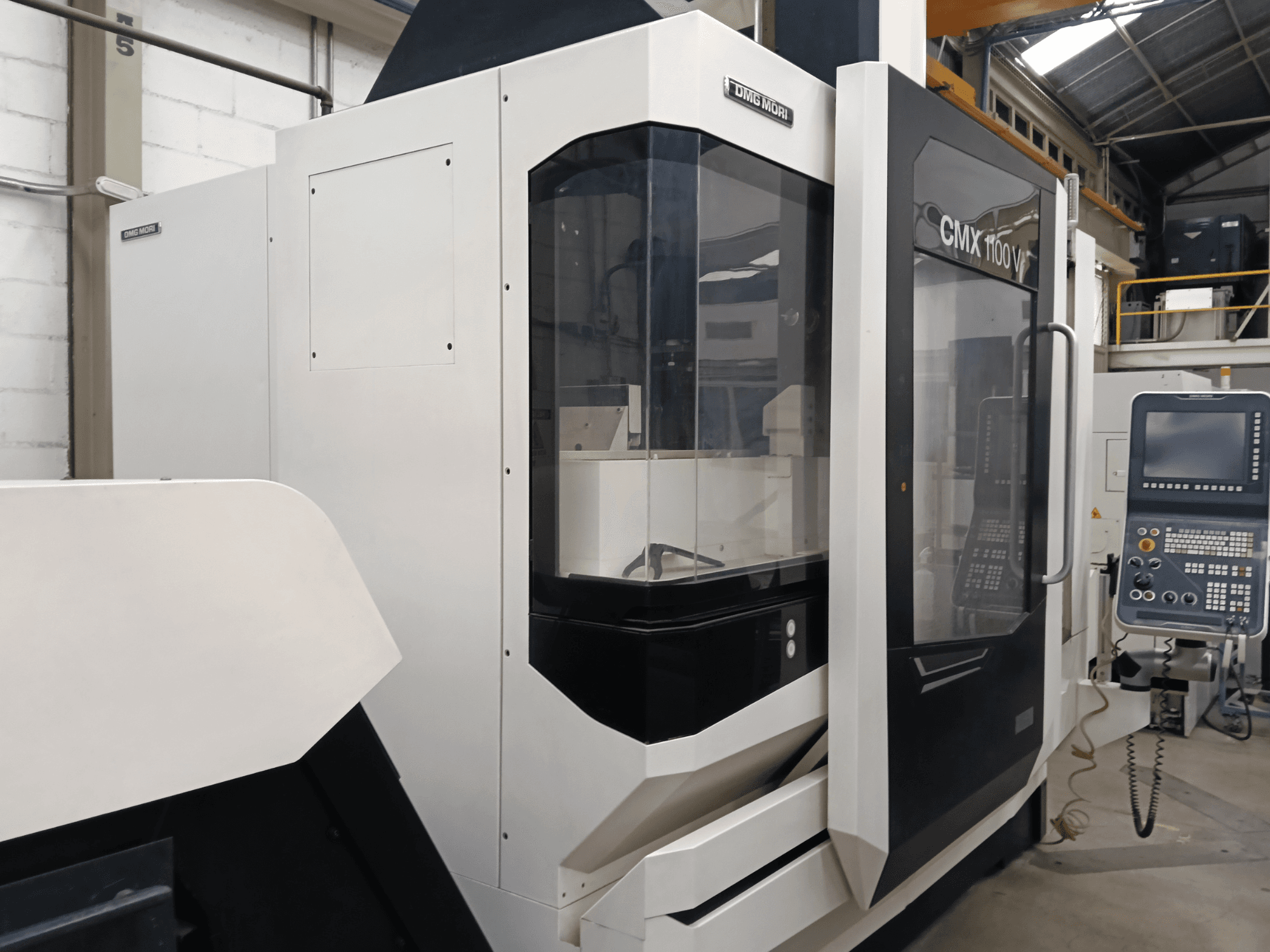 Vertikālais apstrādes centrs DMG MORI CMX 1100 V, skats no priekšpuses, kurā redzams vadības panelis un stikla apvalks.