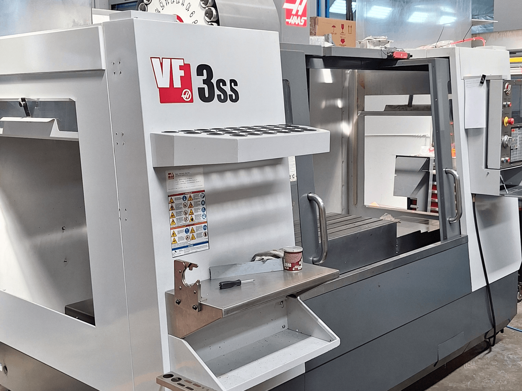 Haas VF-3SS vertikālais apstrādes centrs, priekšējais skats, kurā redzams vadības panelis, instrumentu turētājs un darba zona.